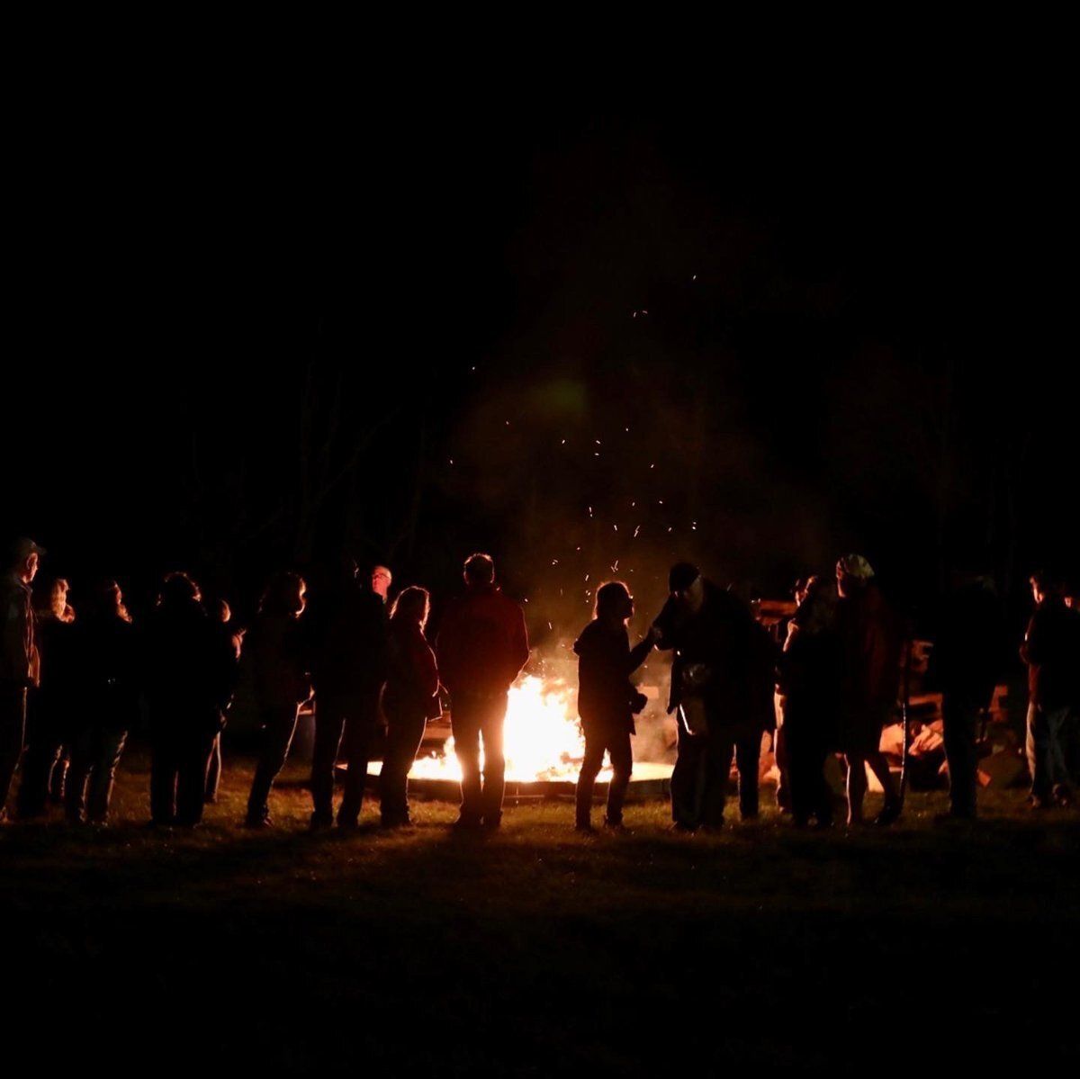 Silhouetted crowd gathered around a bright bonfire at night outdoors