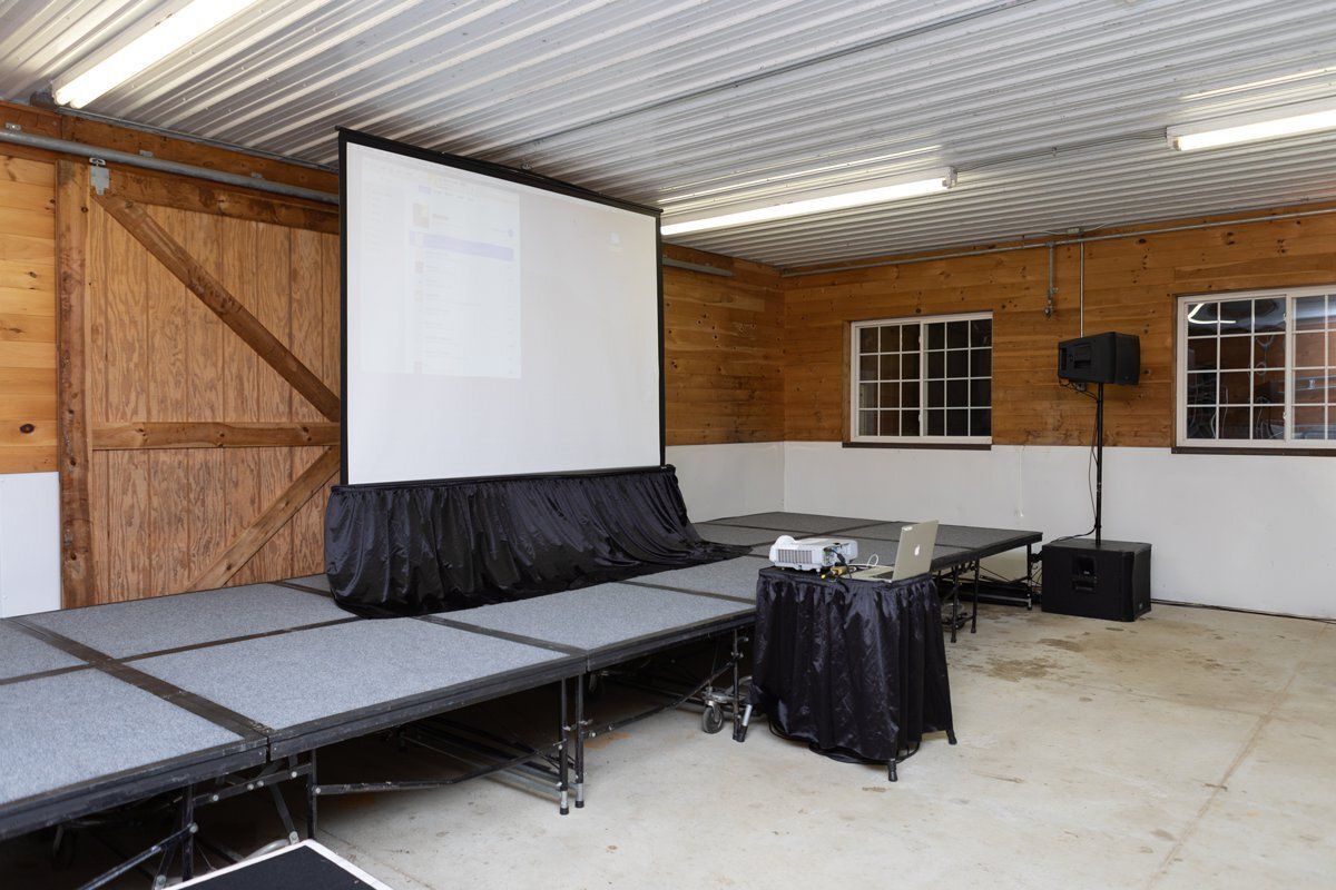 Indoor stage with gray panels, white screen, and black speaker in a covered venue.