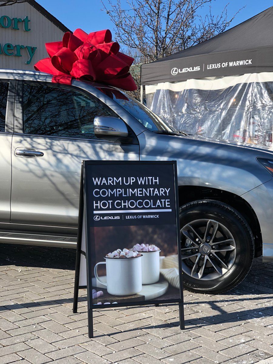 Silver SUV with a red bow beside a sign offering complimentary hot chocolate outdoors