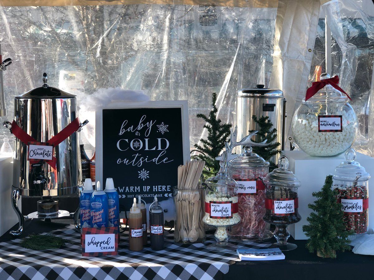 Holiday coffee and cocoa display with jars, cups, and a black chalkboard sign under a clear tent.