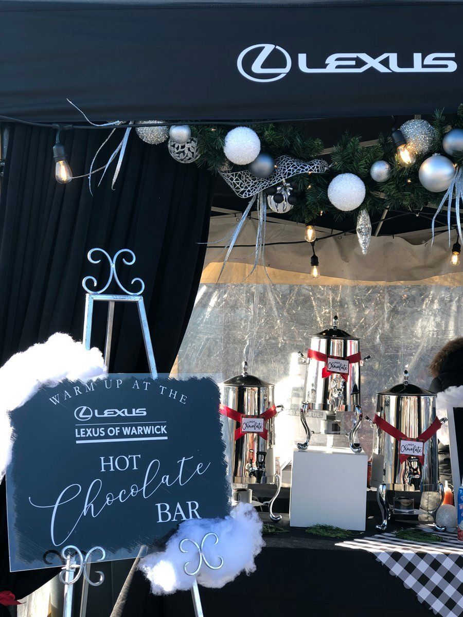 Lexus-branded hot chocolate bar with chalkboard sign, holiday garland, and silver drink dispensers
