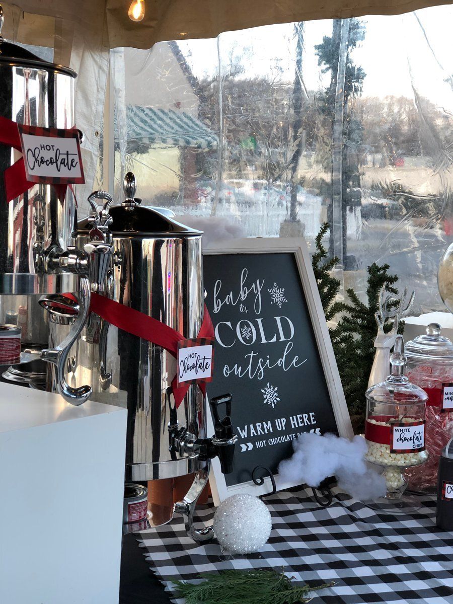 Hot chocolate bar with silver dispensers, chalkboard sign, red accents, and black-and-white checkered tablecloth