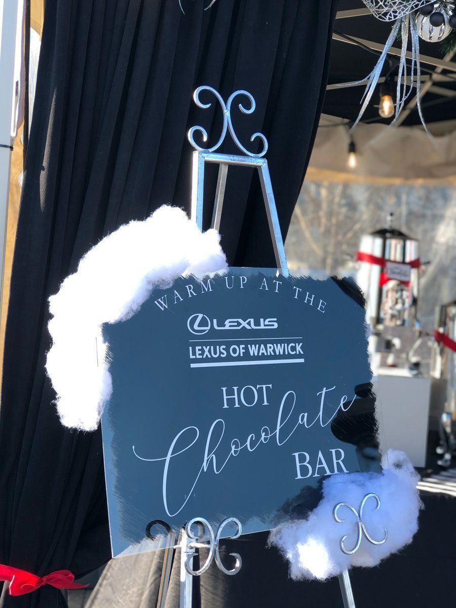 Black sign reading “Hot Chocolate Bar” with white faux snow and a small cup