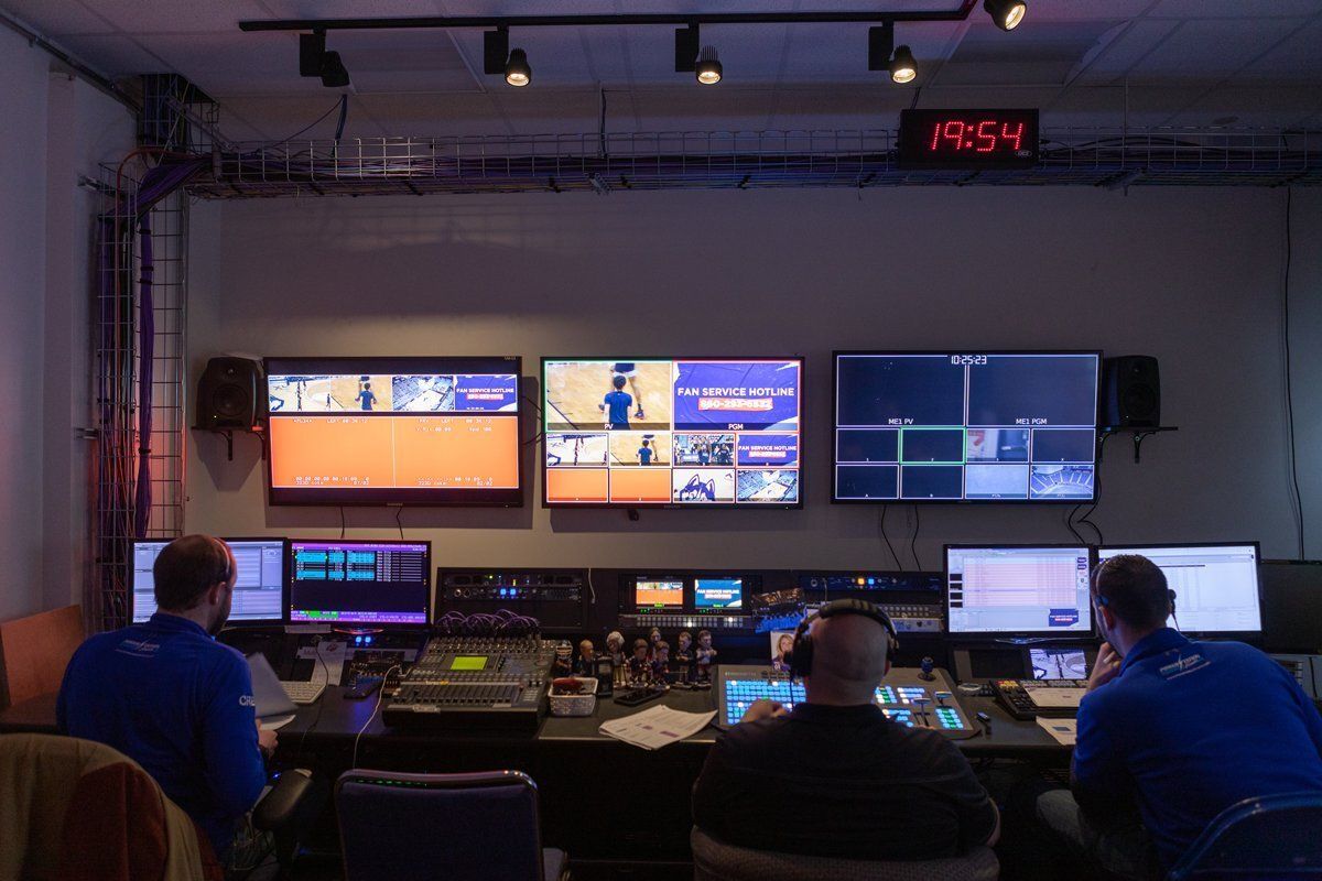 Control room with operators at consoles facing multiple large monitors and status screens.