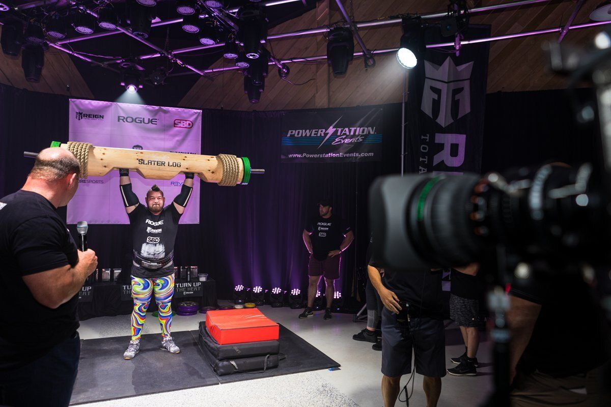 Weightlifter hoists a log overhead on a lit stage during a strongman competition