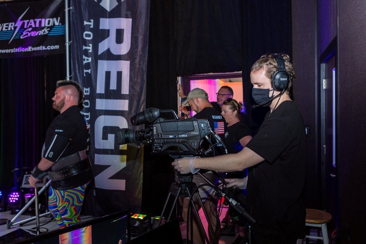 Camera operator filming an esports stage with purple lighting and REIGN banner