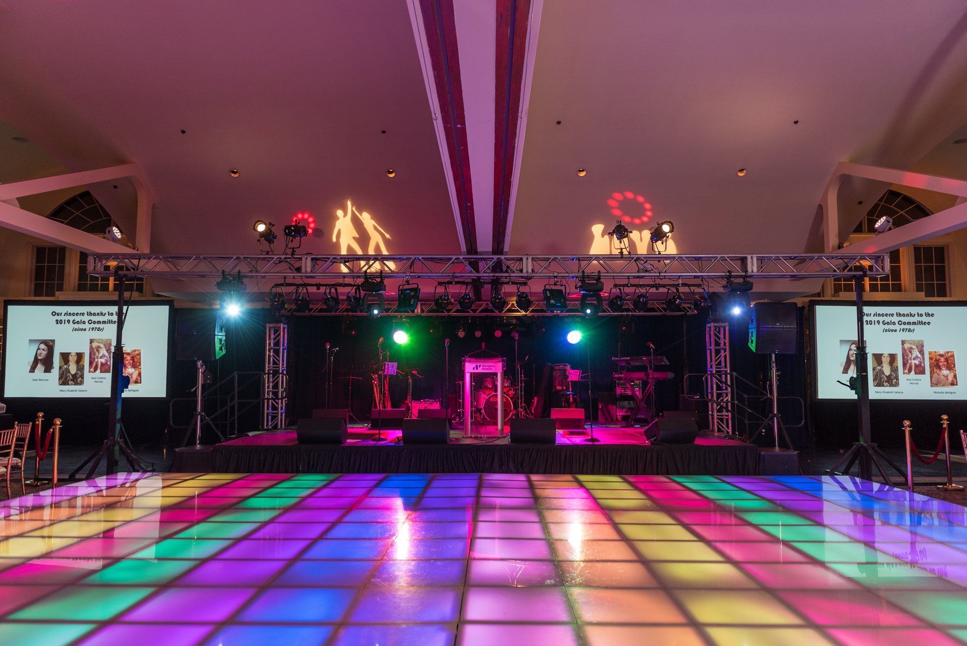 Colorful LED dance floor and stage setup in a large event hall with lighting trusses and screens
