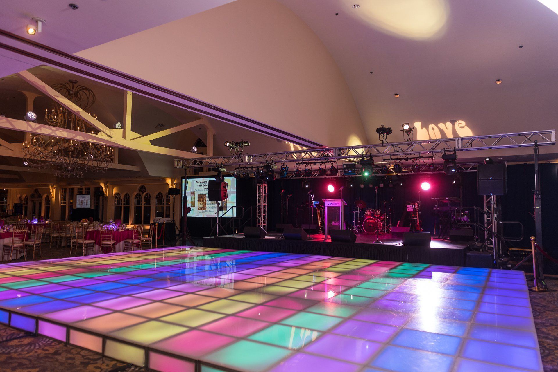 Empty event hall with a glowing multicolor dance floor and pink stage lights at night