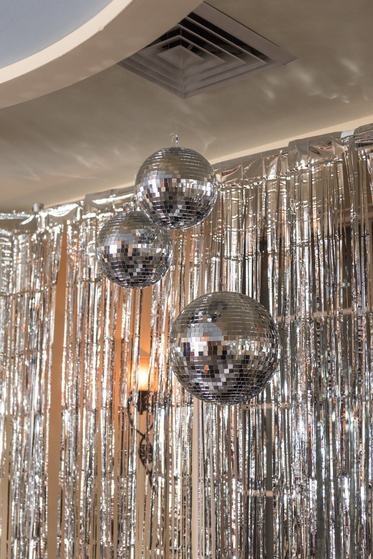 Silver disco balls hanging in front of a metallic fringe curtain indoors