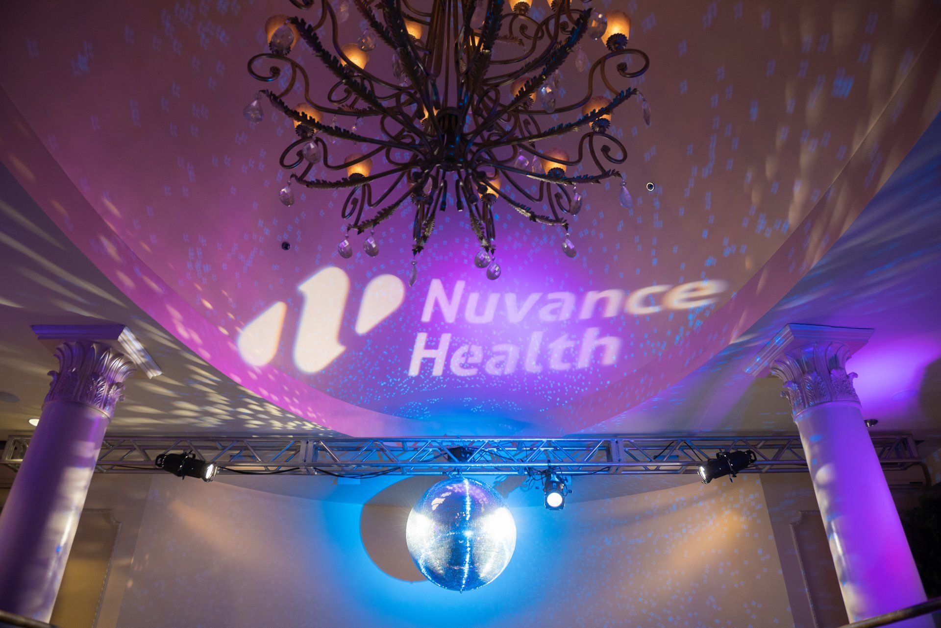 NuVance Health logo projected in purple light on a decorated event ceiling