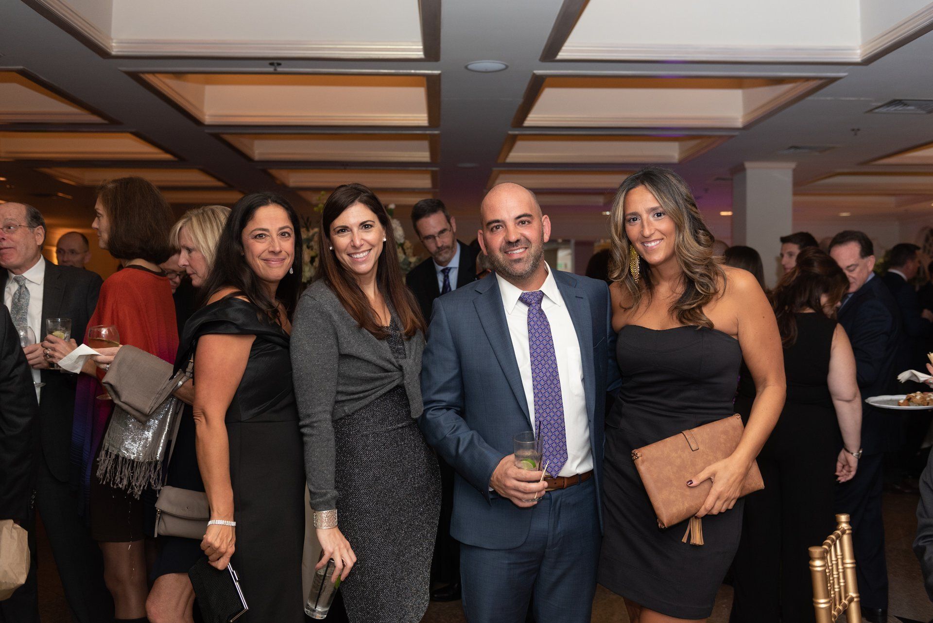 Four people posing at a formal indoor event, dressed in black and gray evening attire.