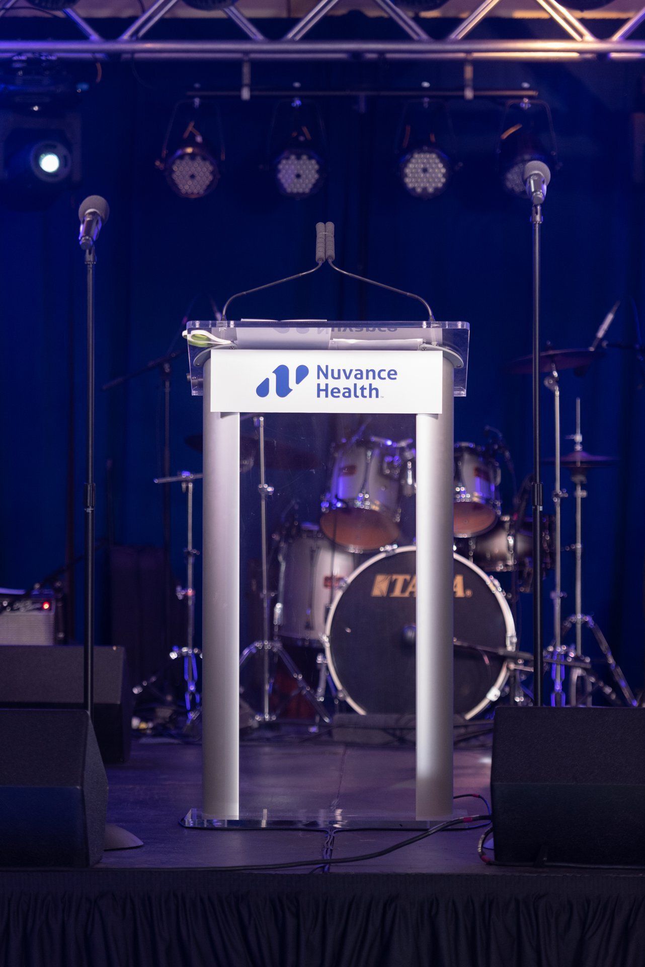 Empty podium on a stage with a drum kit and microphones under blue lighting