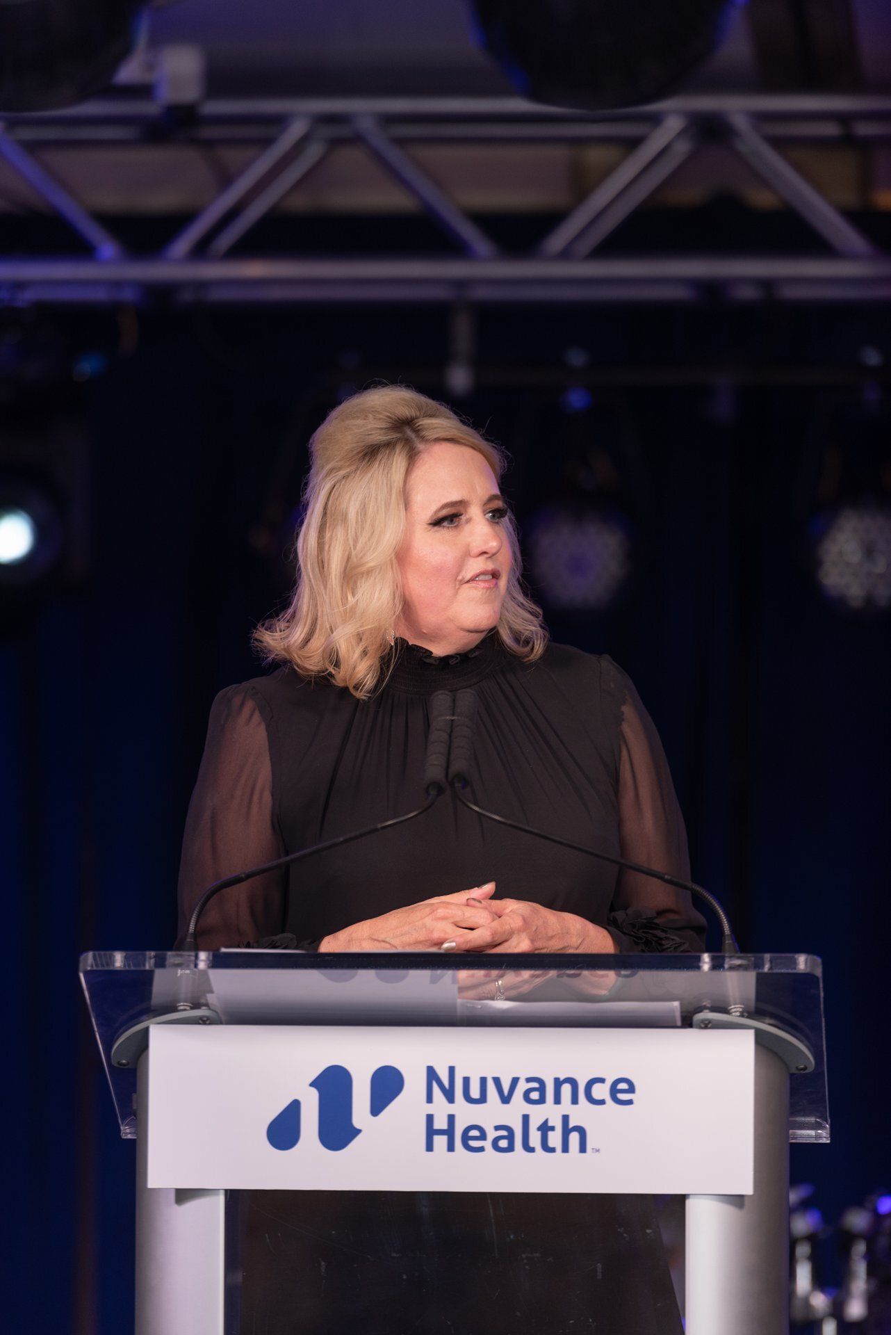 Woman speaking at a podium with a Nuance Health sign onstage, looking to her left.