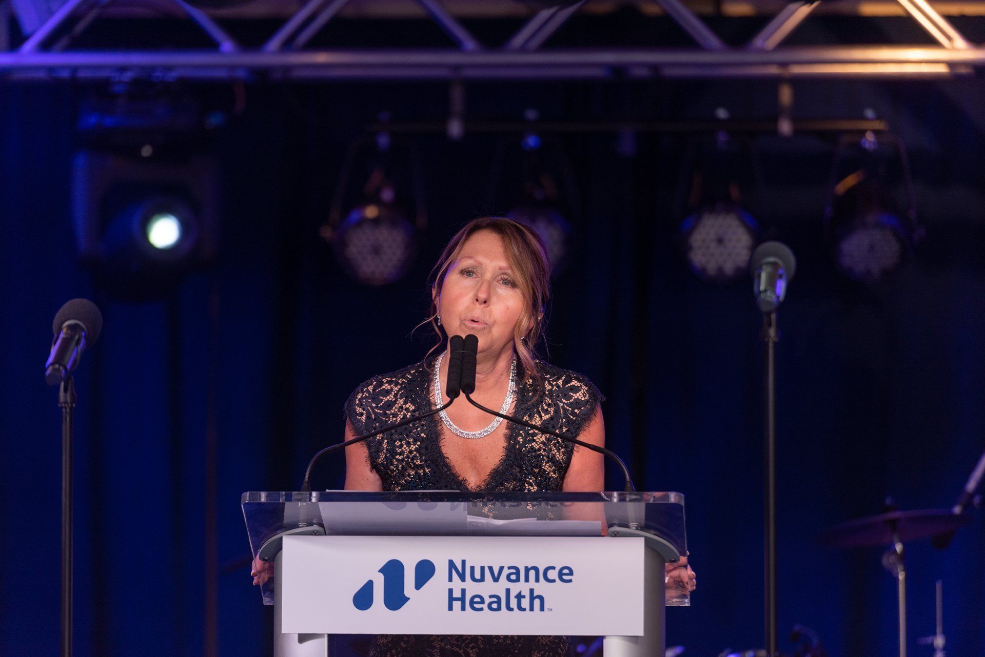Speaker at a podium with a Nuance Health sign, speaking on a stage under blue lighting