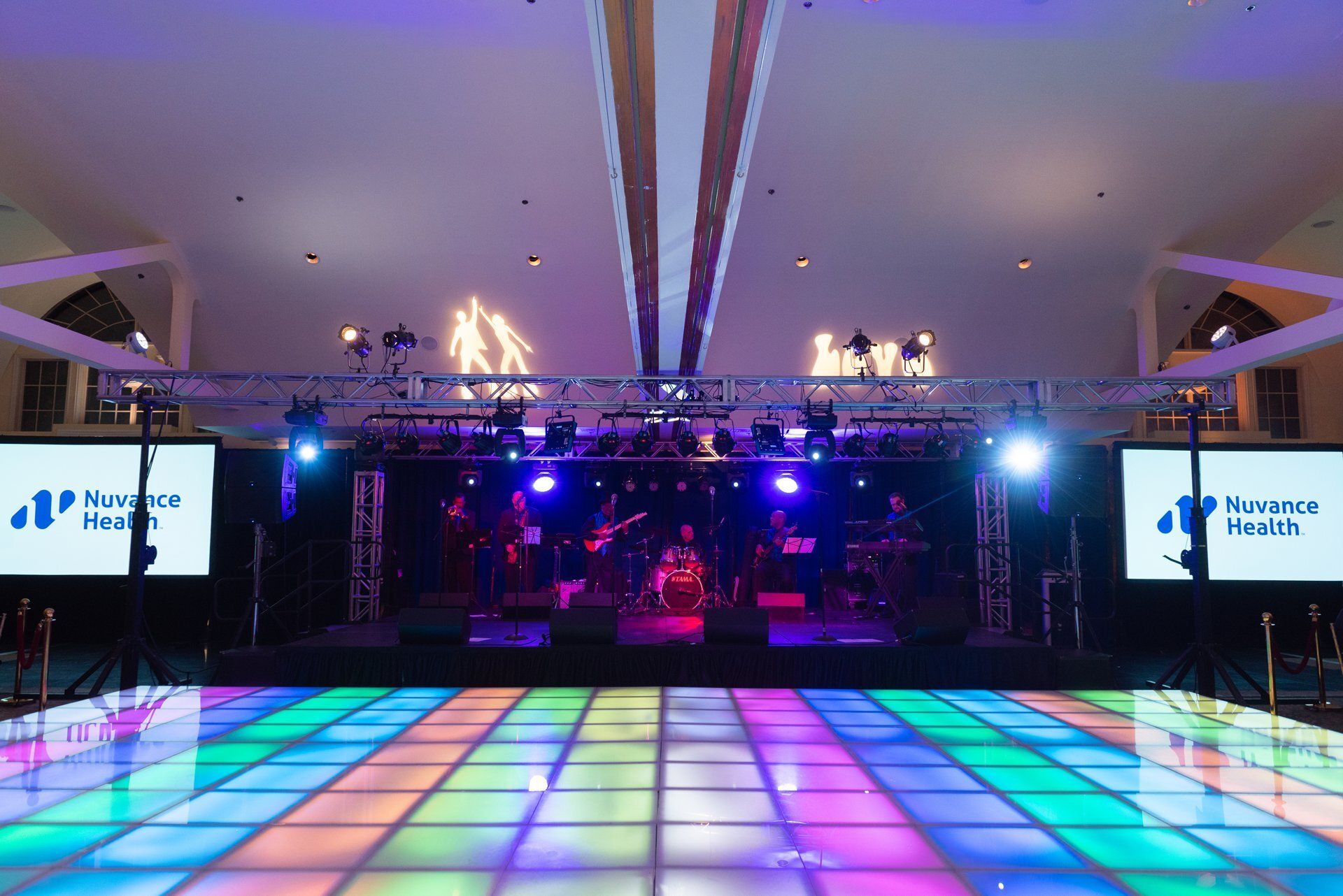 Colorful LED dance floor in a large event hall with stage lighting and screens reading “Himansh Health”