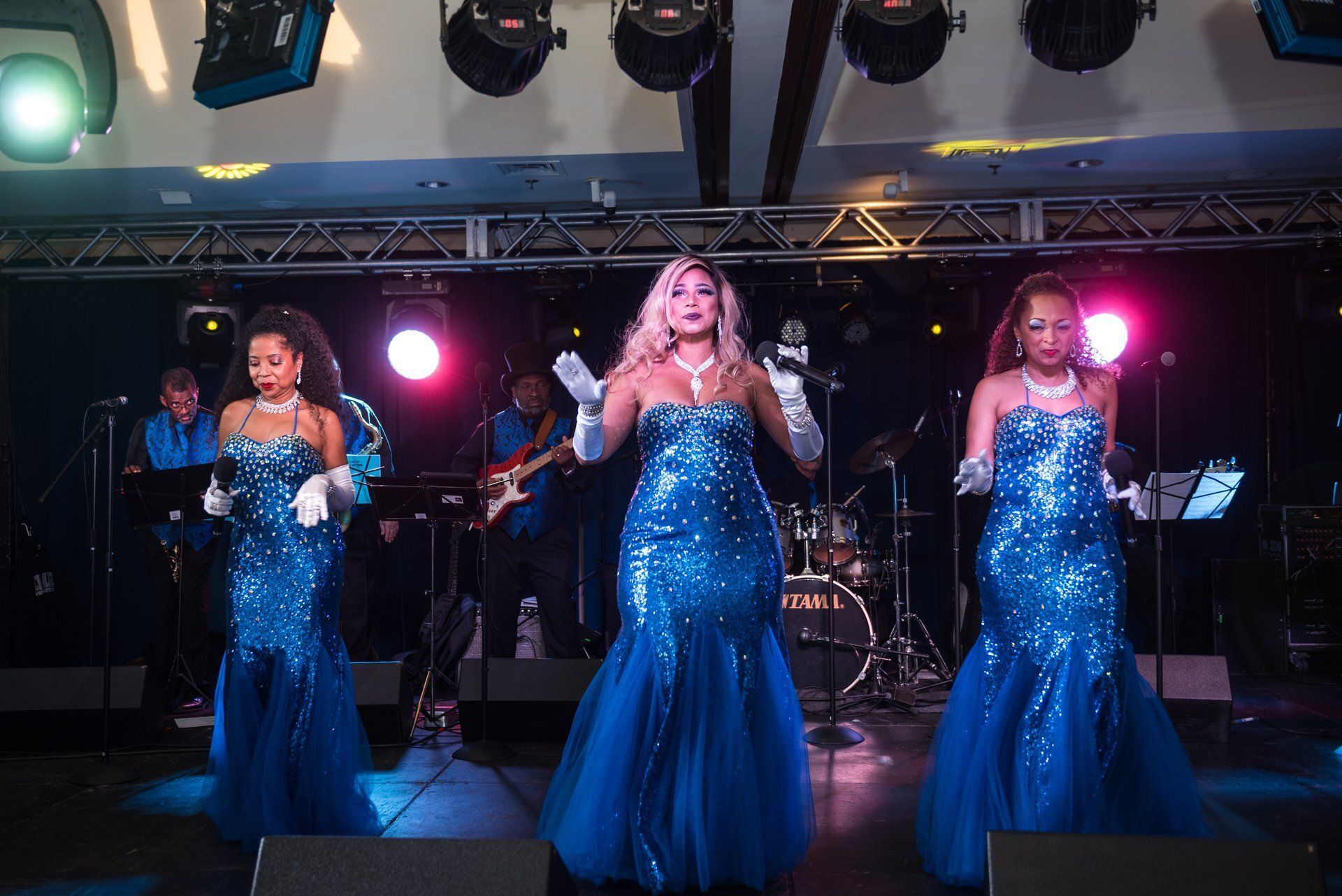Three singers in blue gowns performing on a stage with bright lights
