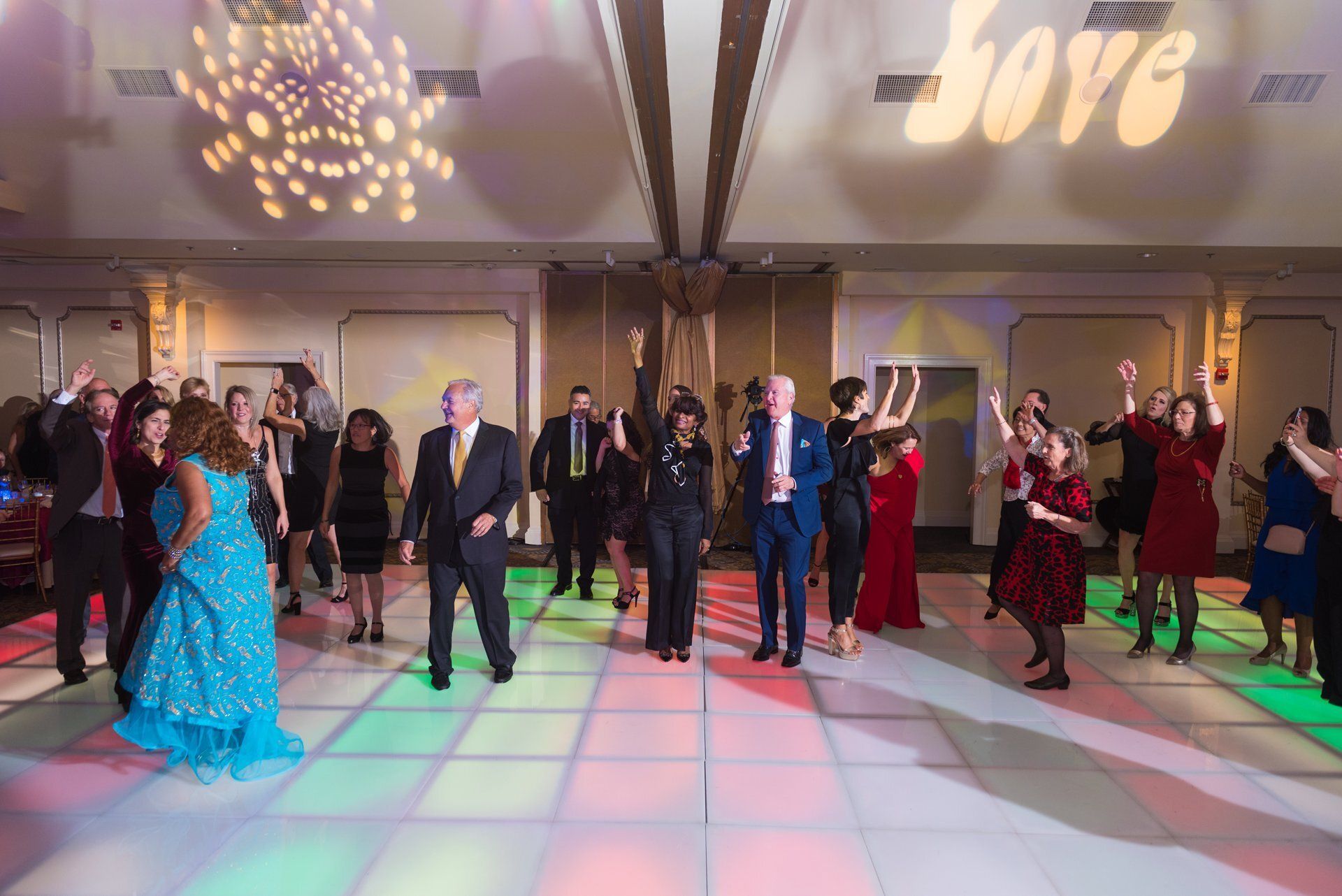 Guests dancing at a formal indoor event under colorful floor lighting and a projected logo