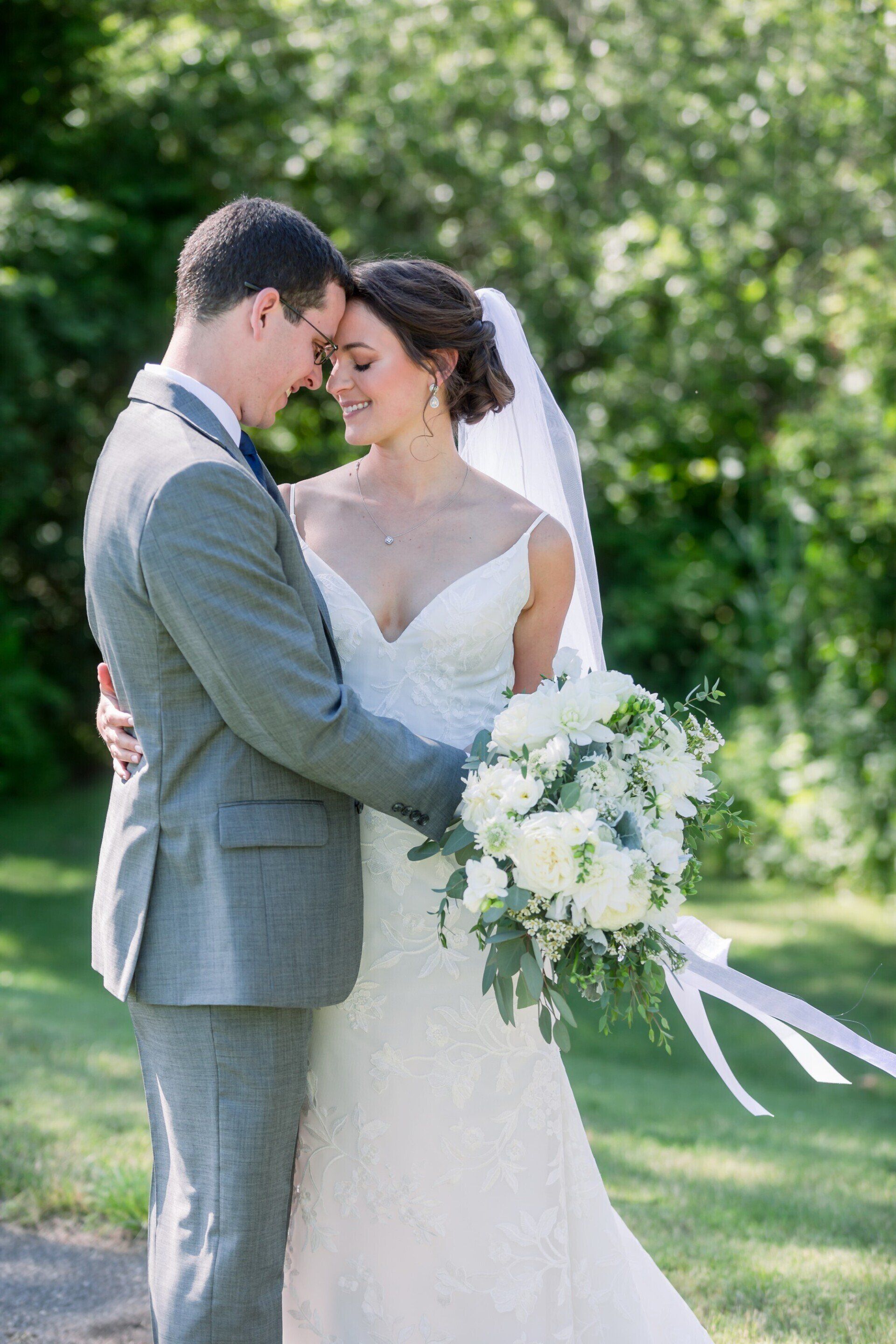 Bride and groom embracing outdoors, holding a white bouquet in a sunlit garden