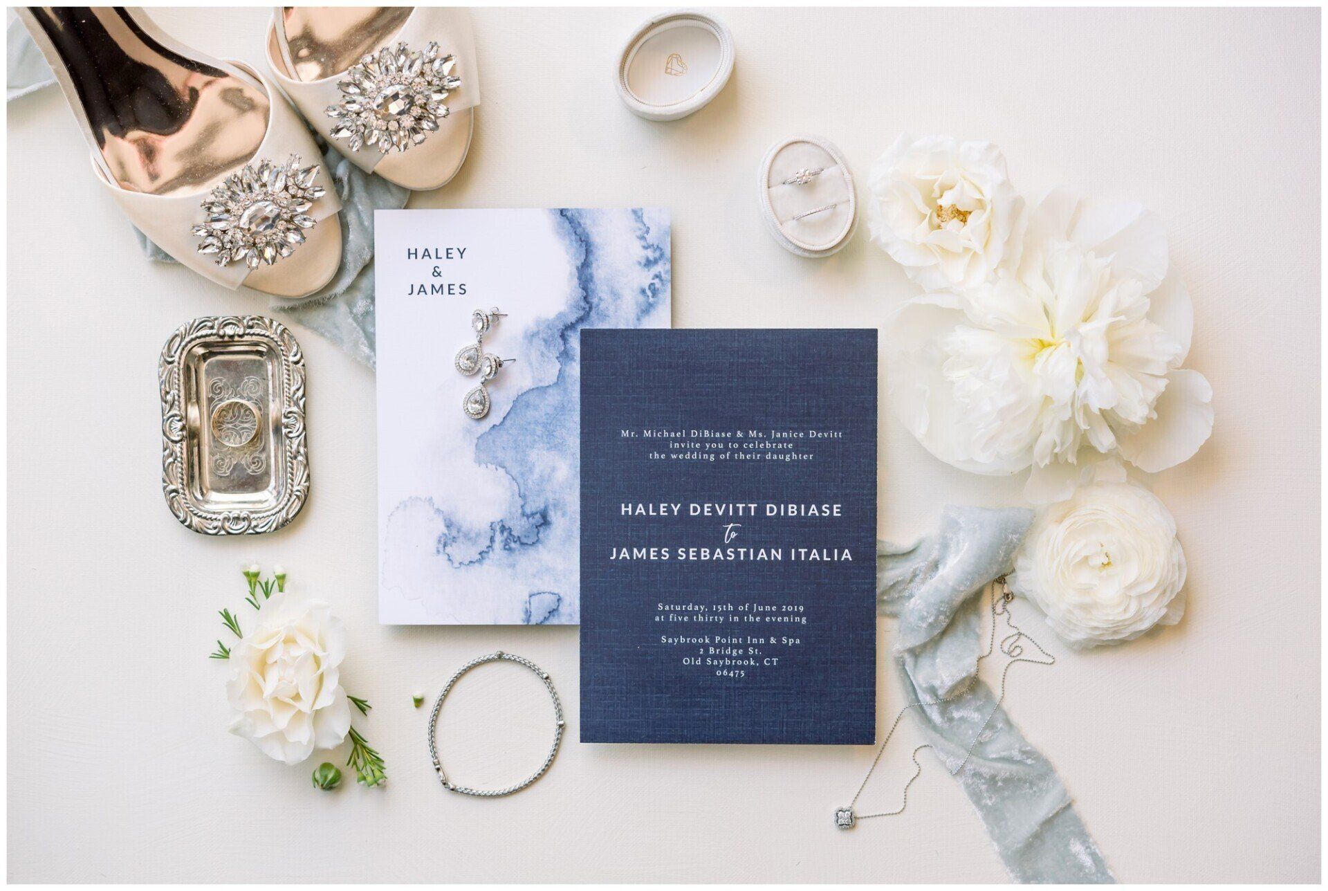 Flat-lay of wedding stationery with white flowers, jewelry, and elegant accessories on a light background