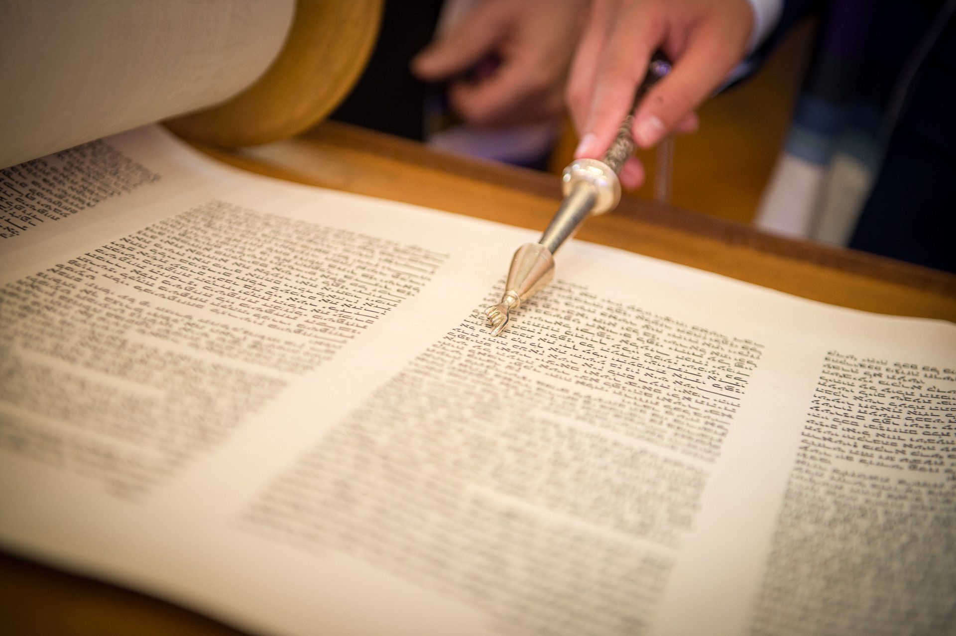 A hand uses a small brush to turn pages of a large open book under warm light.