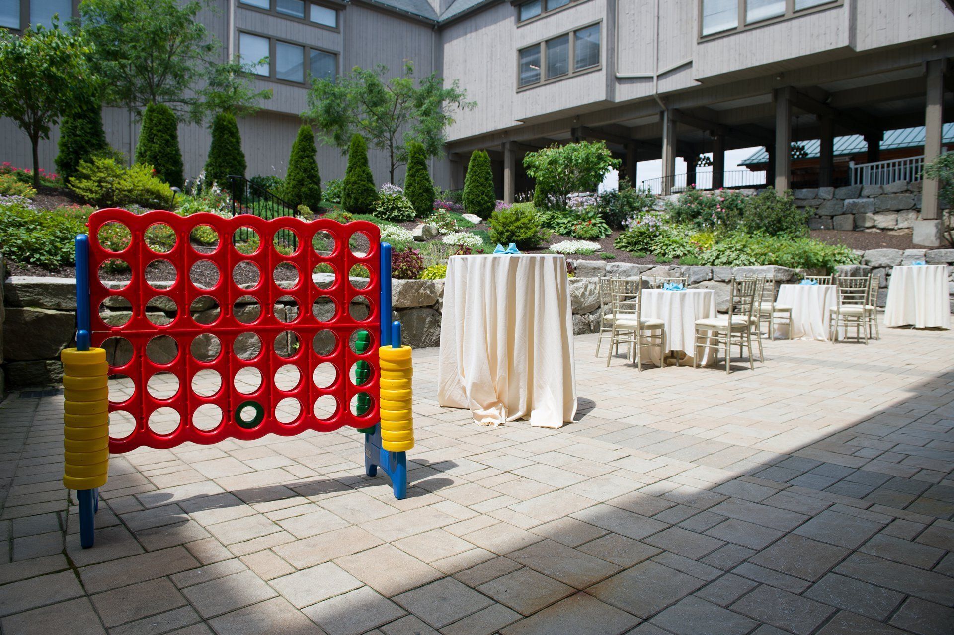 Outdoor terrace with a giant red-and-yellow Connect Four game near café tables and chairs