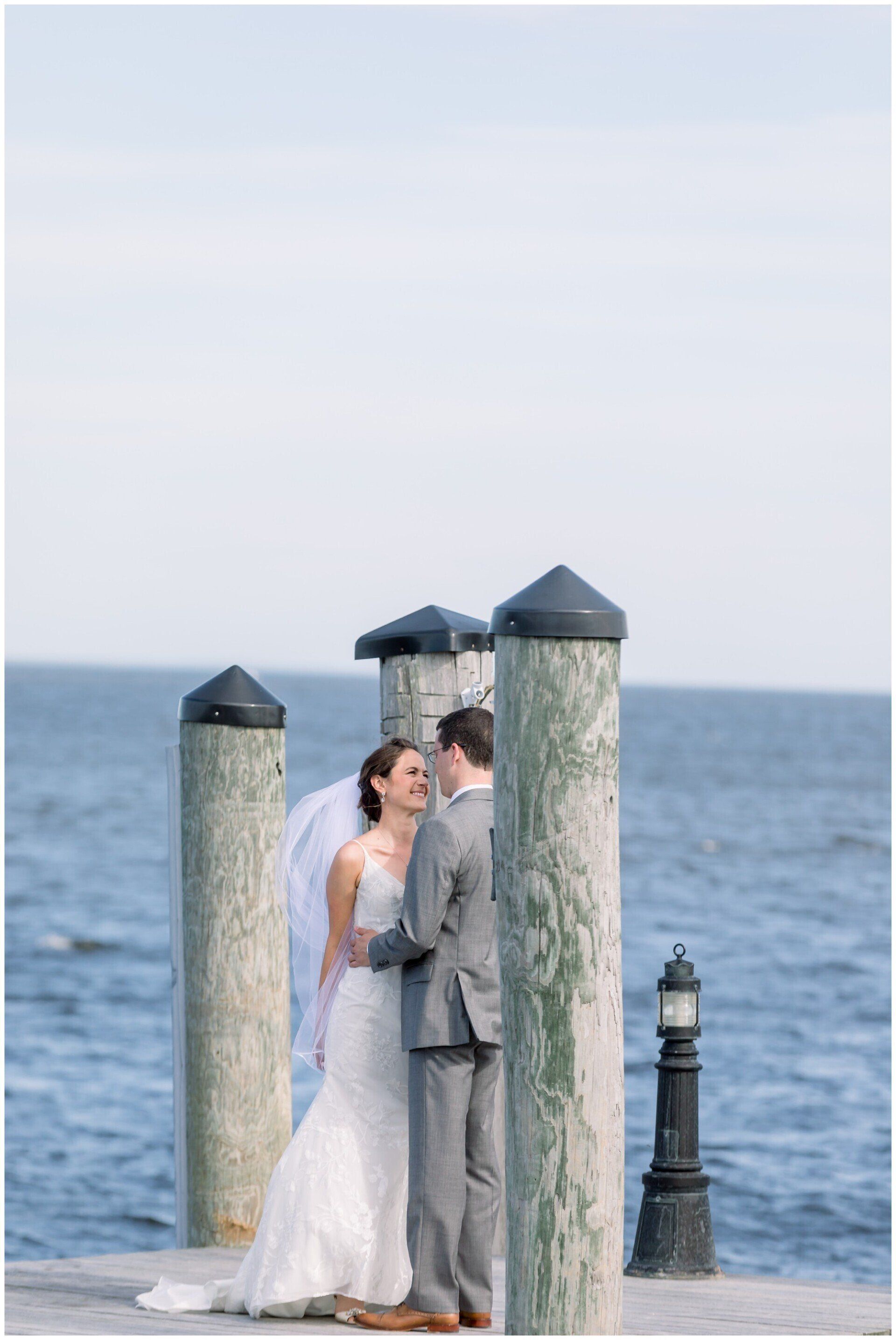 Bride and groom embracing by weathered dock posts beside the ocean