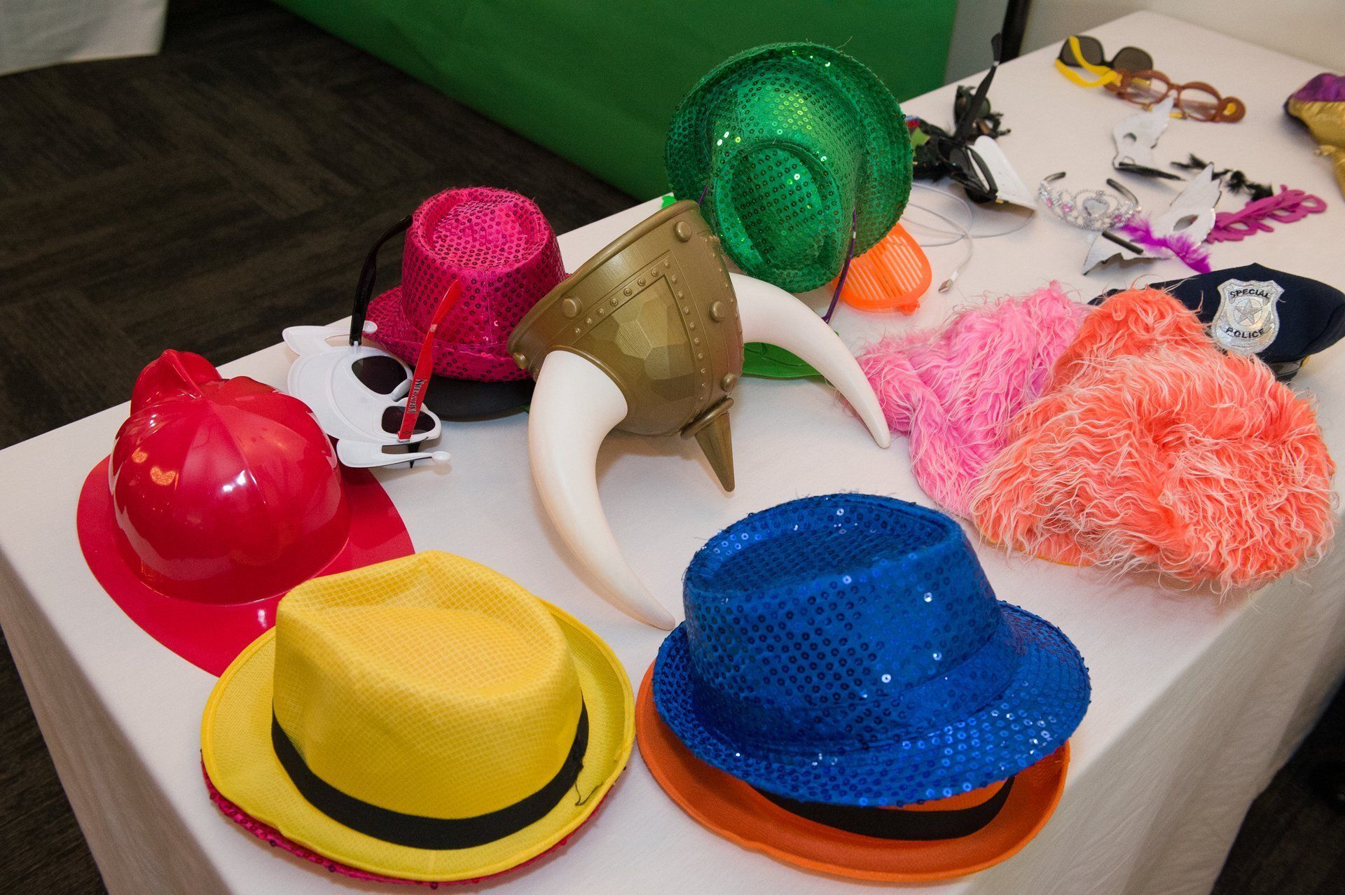 Colorful party hats and wigs scattered on a table, including red, green, blue, yellow, and pink items.