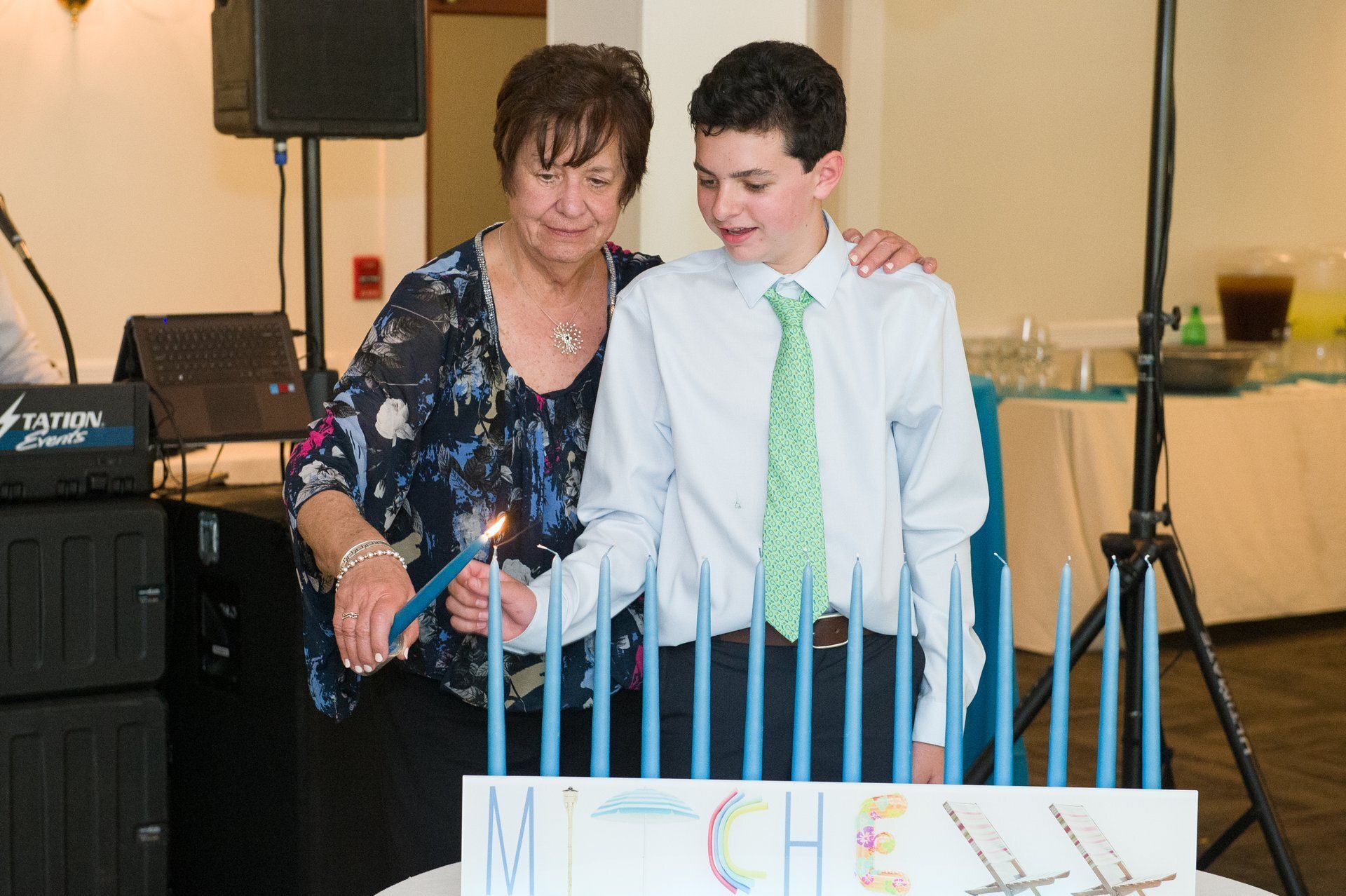 Woman and boy standing behind a birthday cake, looking at candles in a decorated indoor party setting