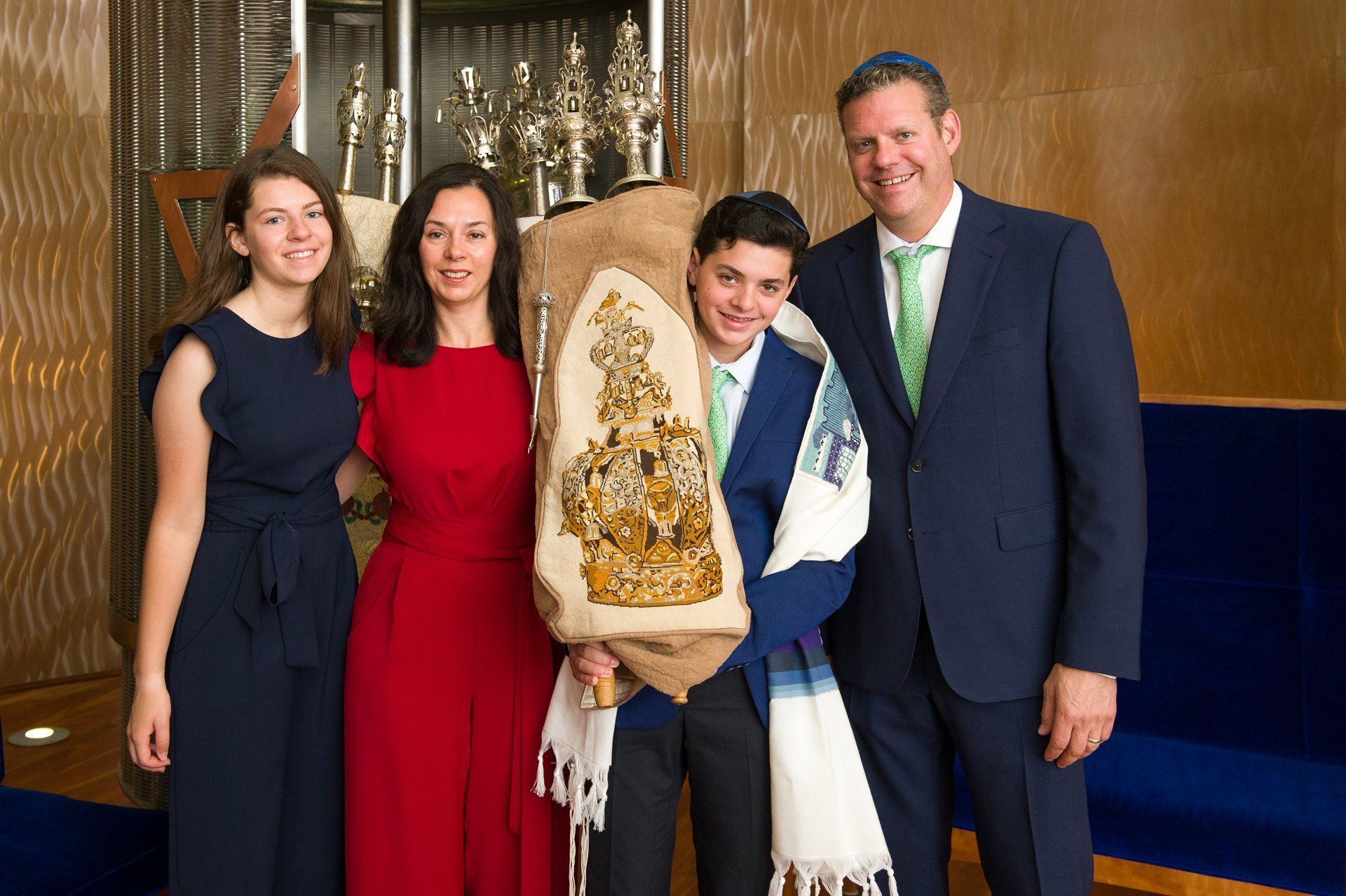 Four people posing indoors, one holding a decorated award and wearing a white scarf.