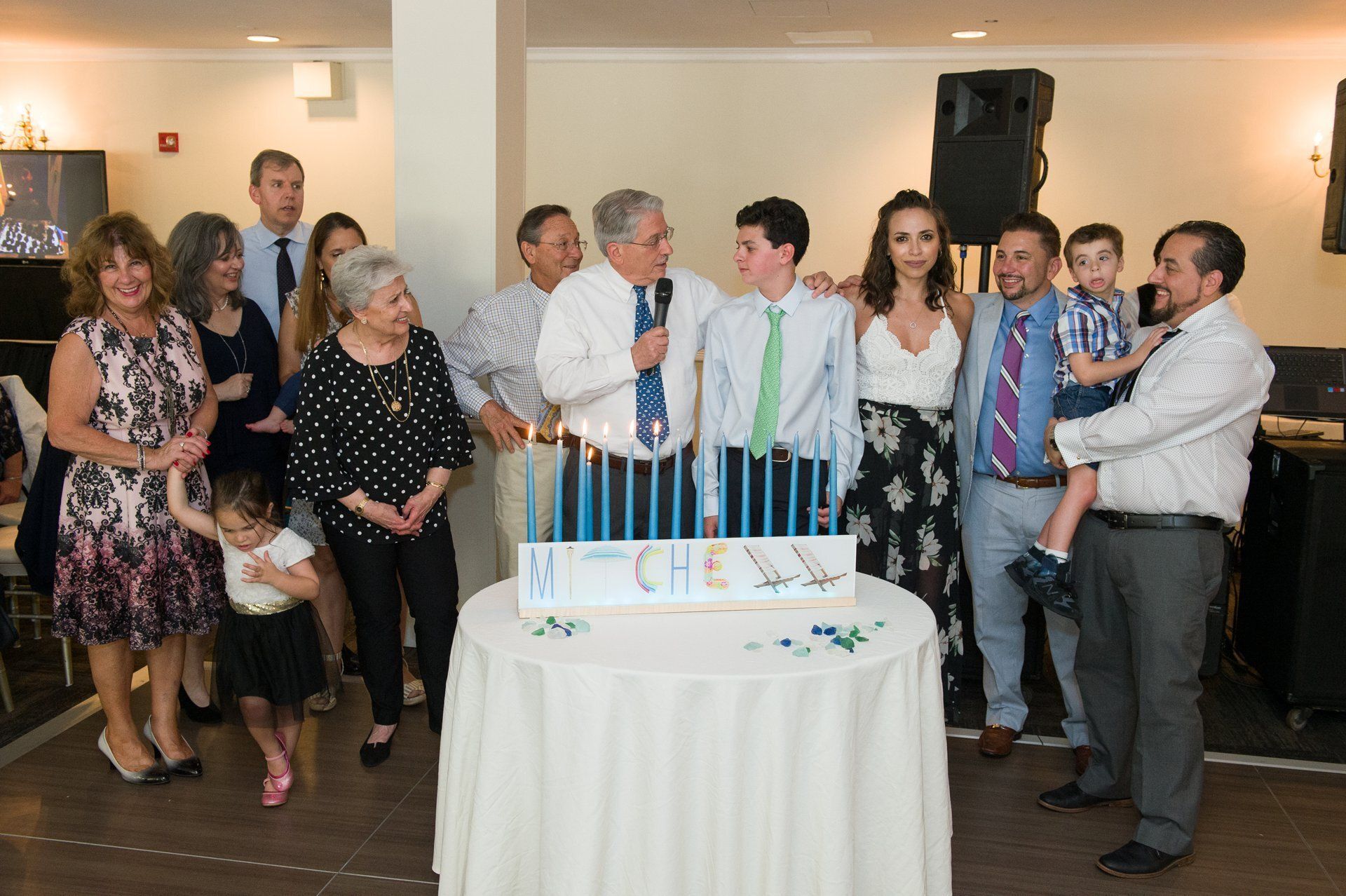 People gathered around a birthday cake with blue candles at a party indoors.