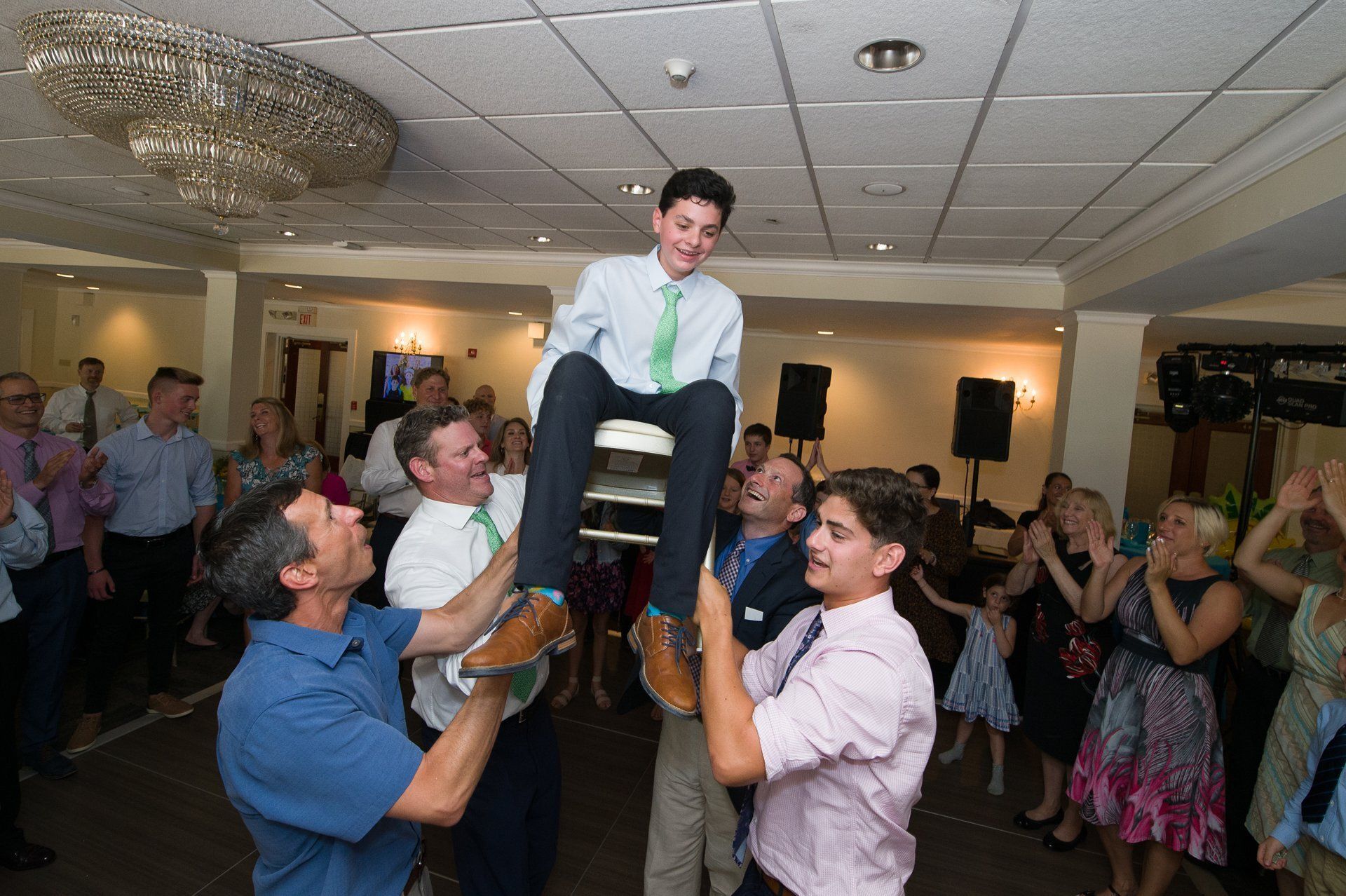 Person being lifted on shoulders during a lively indoor celebration, with guests clapping around them