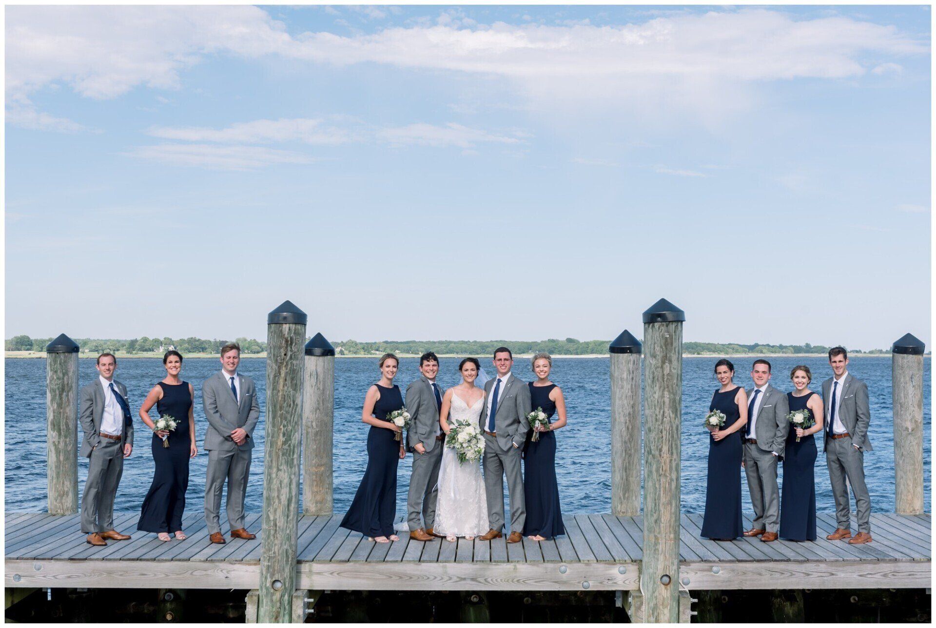 Group of people posing on a dock by the water under a blue sky