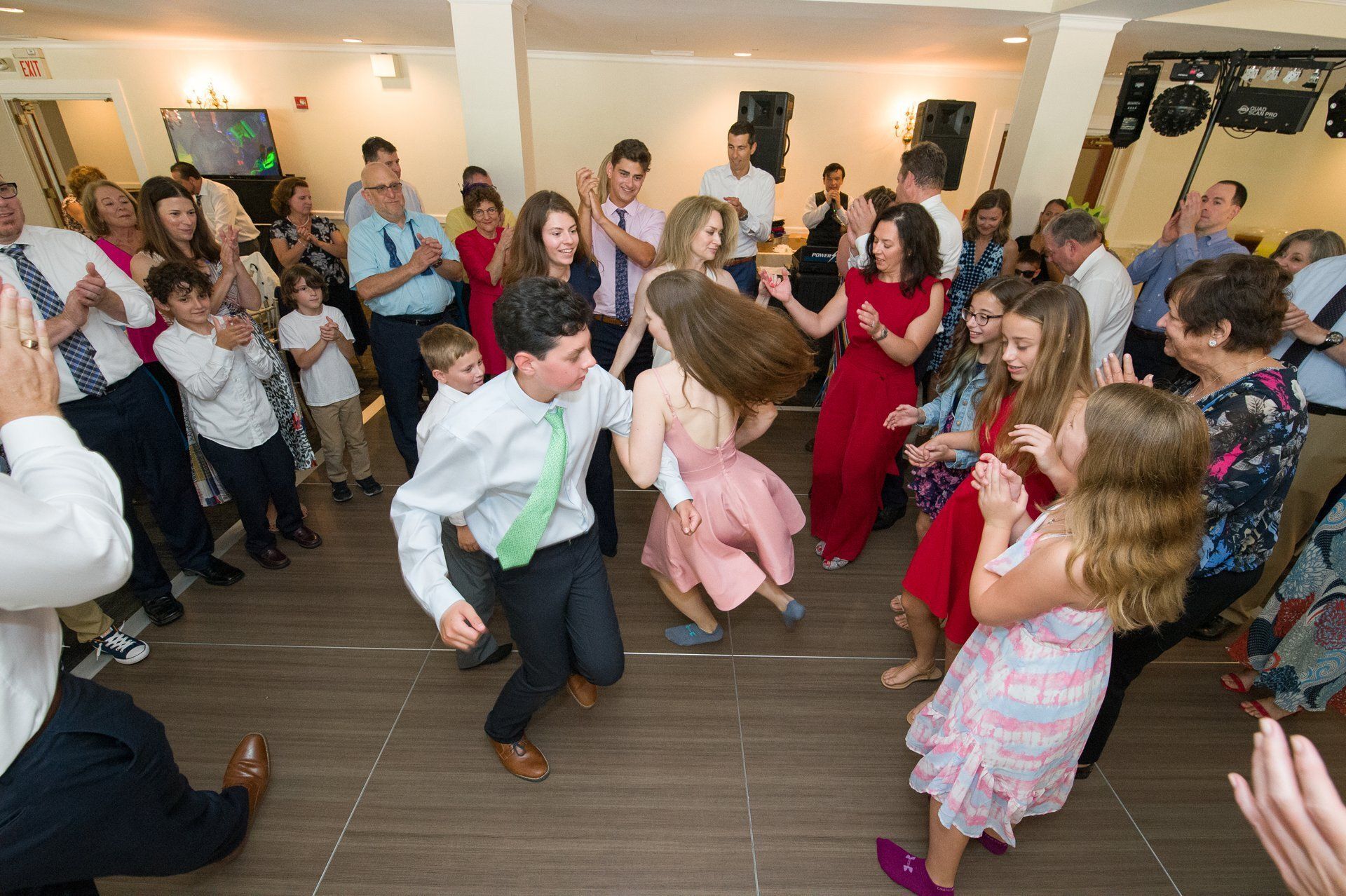 People dancing at a lively indoor party, with guests clapping and smiling around them.