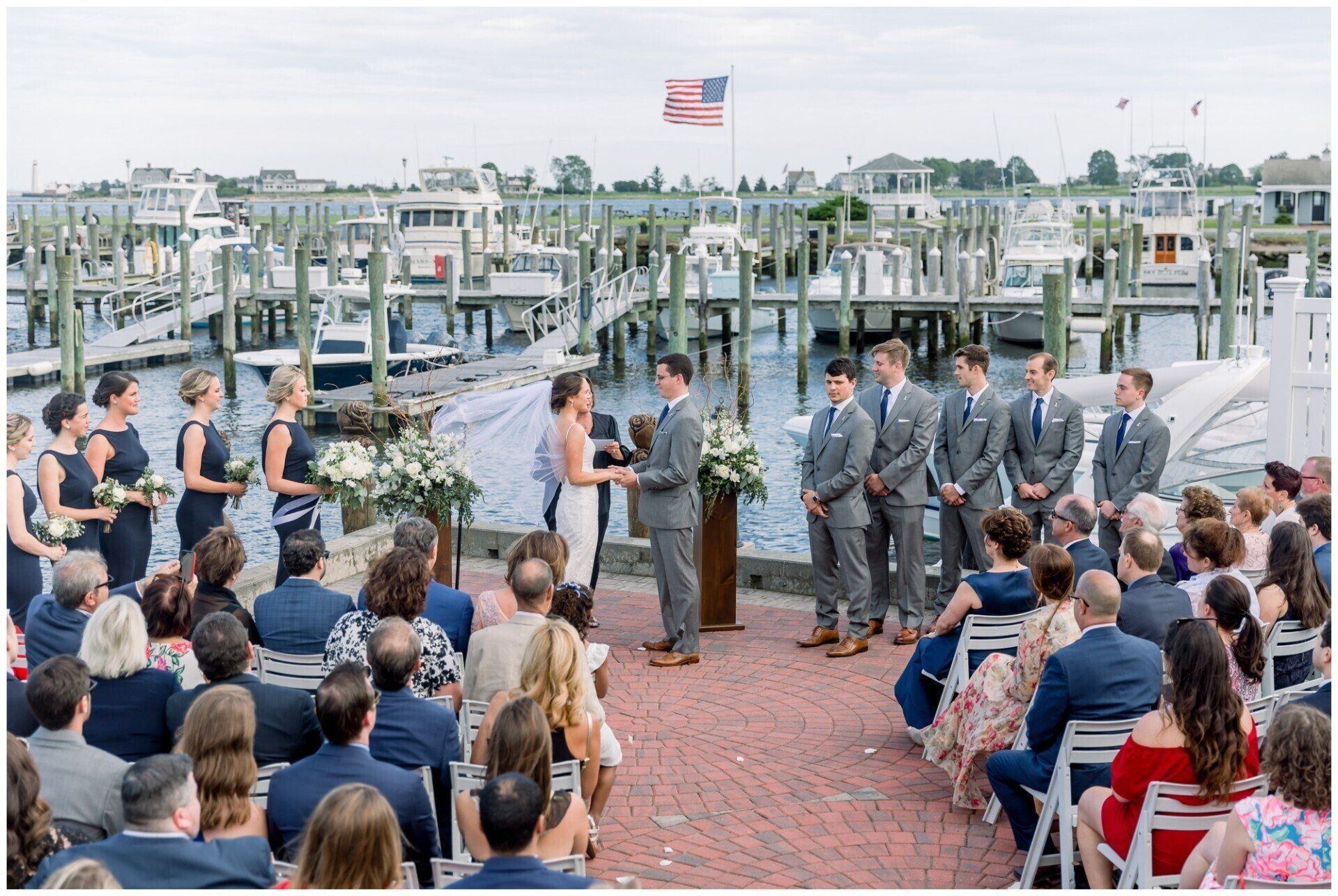 Outdoor wedding ceremony at a marina, with bride and groom at the altar surrounded by seated guests and boats behind them