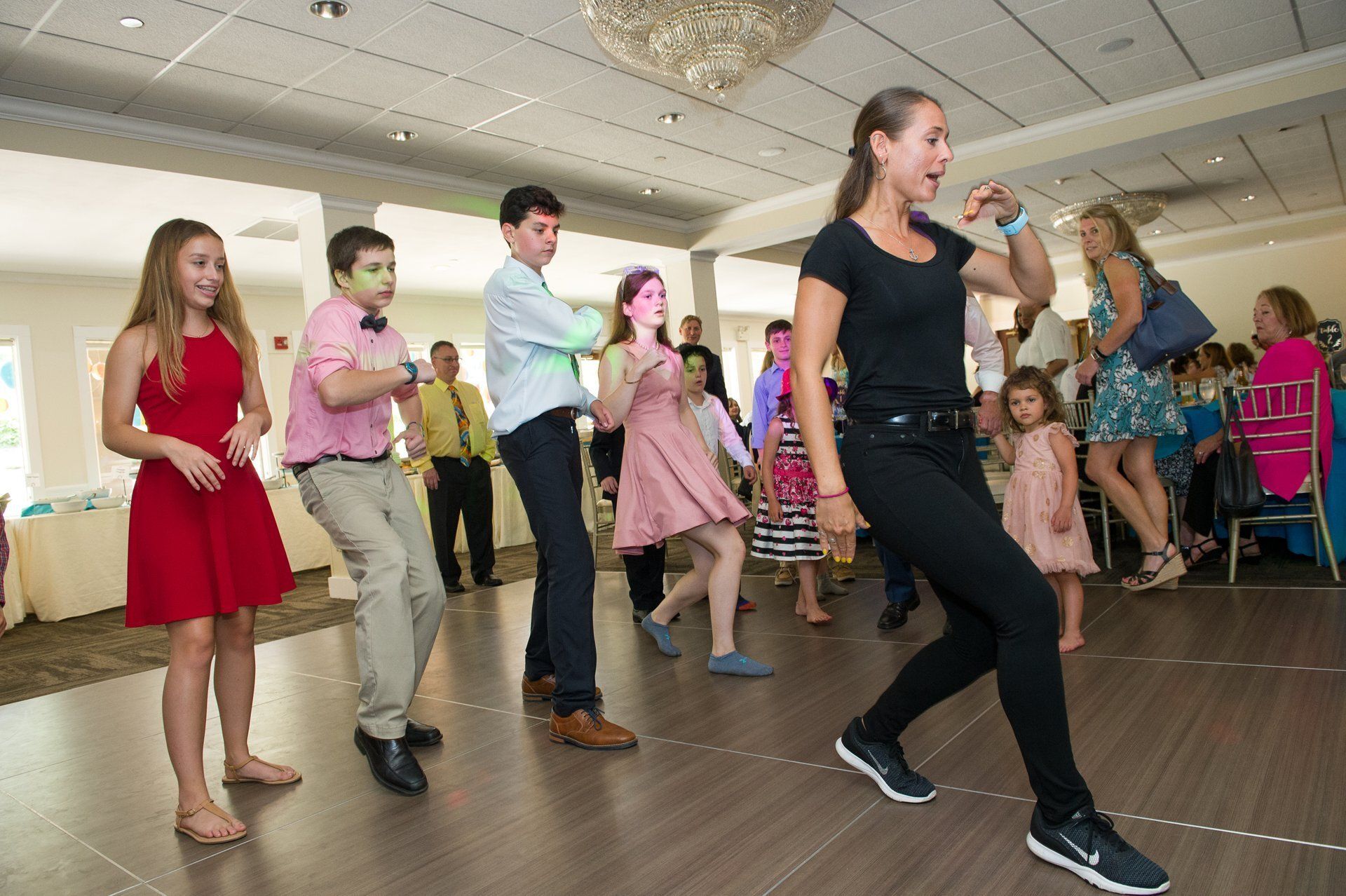 People dancing at a lively indoor party with balloons and guests seated nearby
