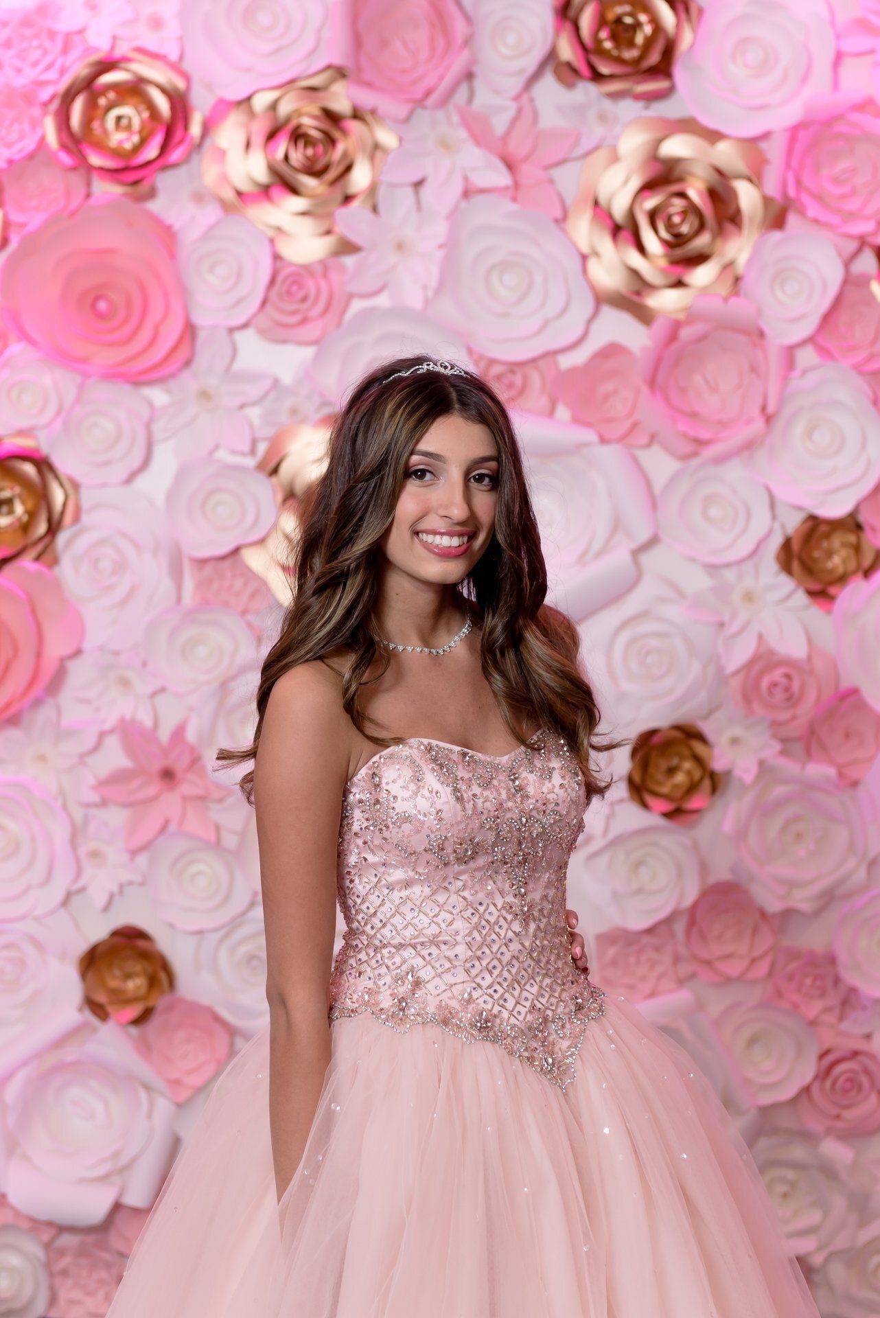 Woman in a pink sequined gown posing against a pink floral backdrop