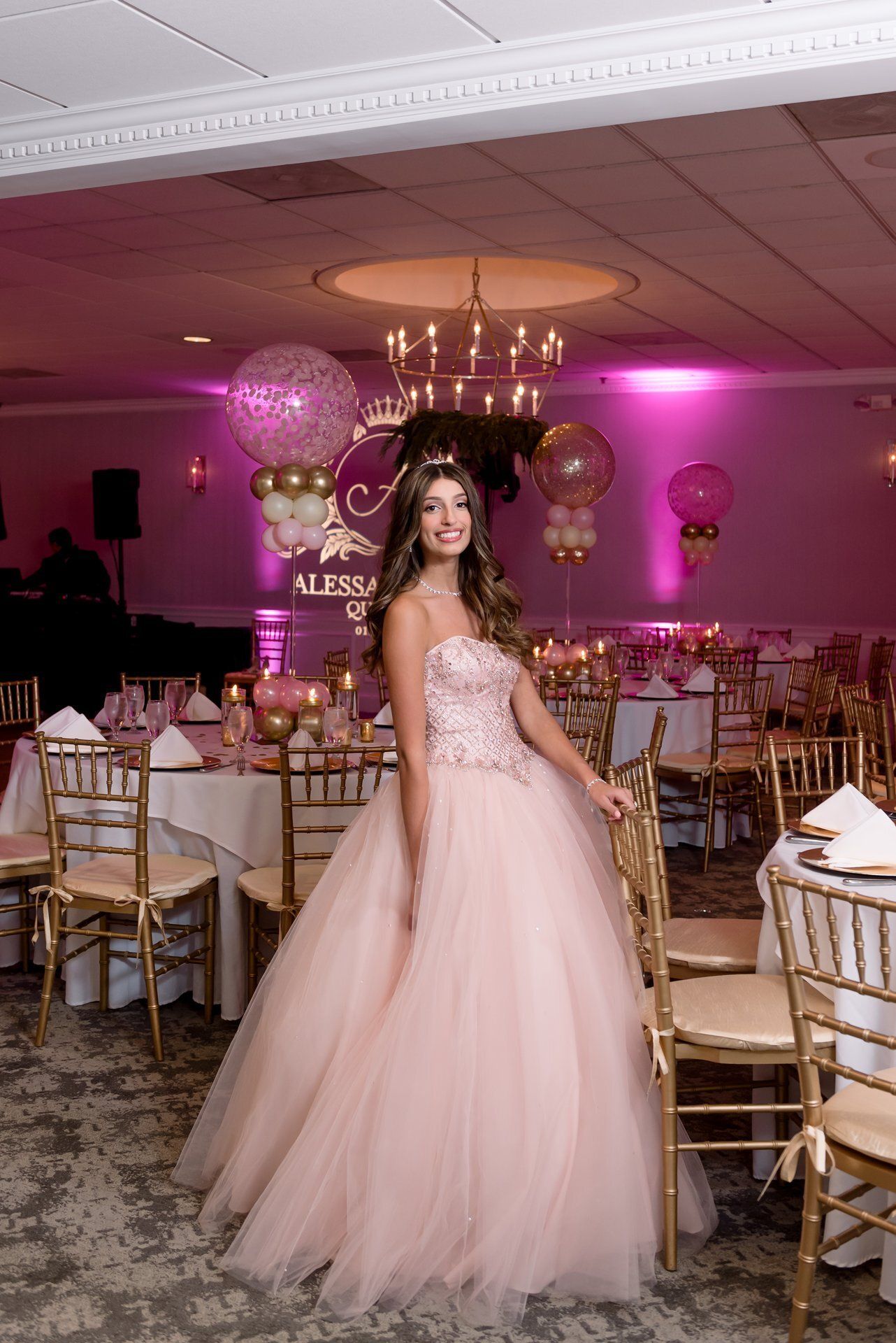 Woman in a pink gown standing in a decorated banquet hall with gold chairs and pink lighting