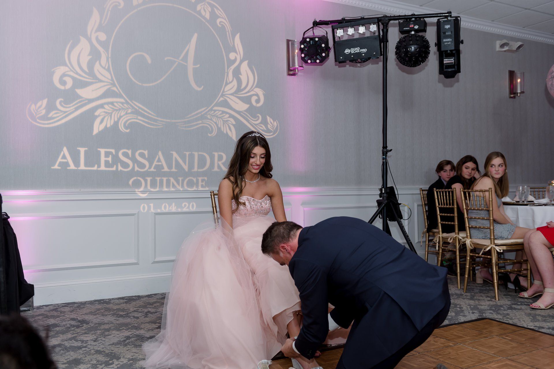 Bride in pink gown at a wedding reception while a man adjusts her dress on the dance floor.