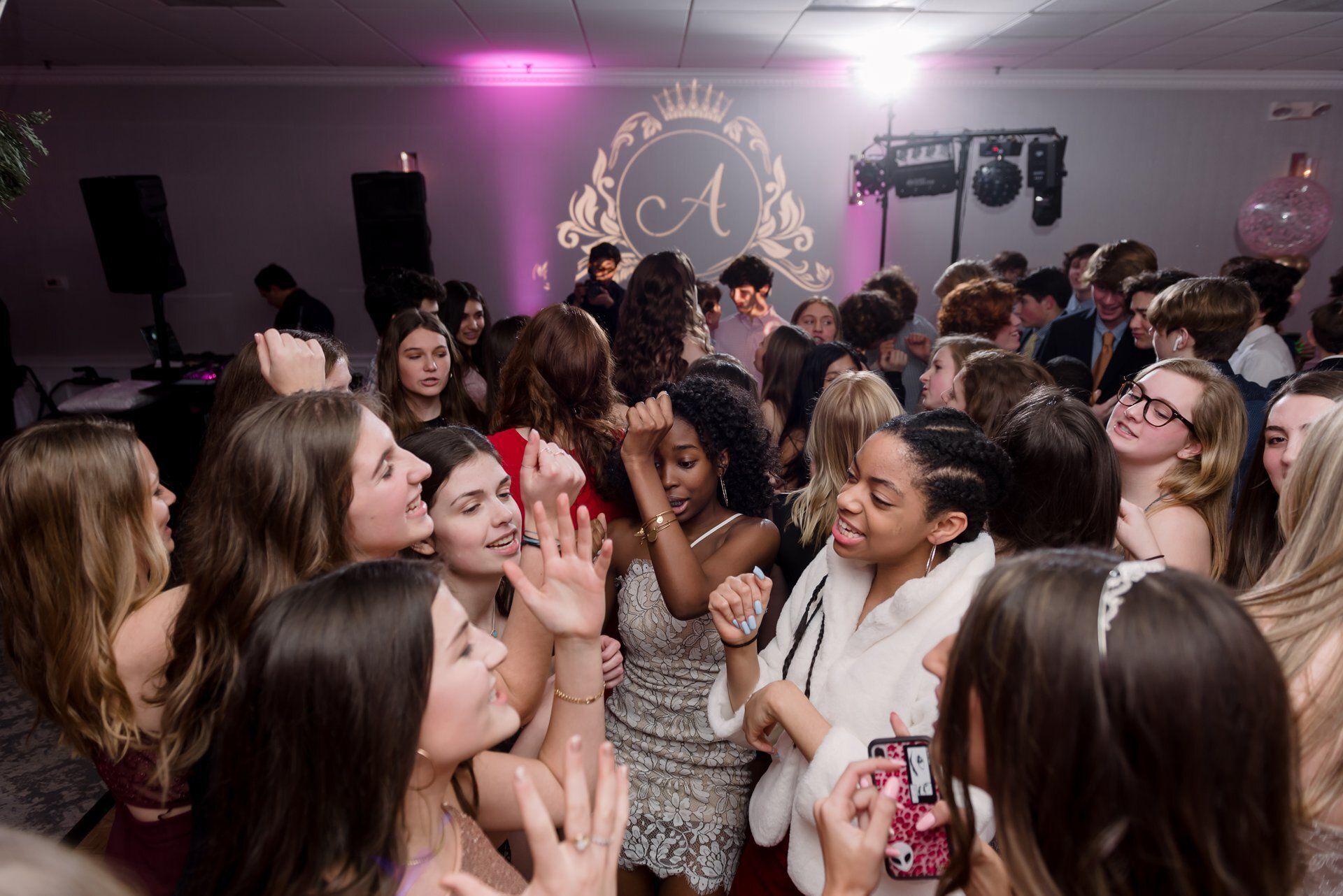 Crowded party scene with people dancing and chatting under pink lighting and disco lights