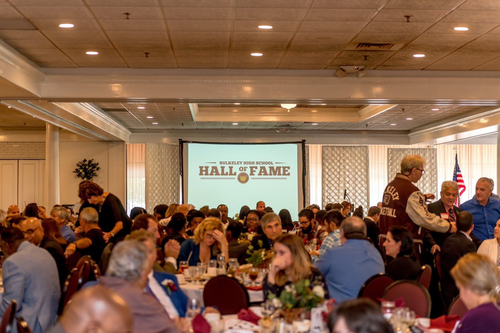 Banquet hall audience watching a Hall of Fame presentation on a large screen