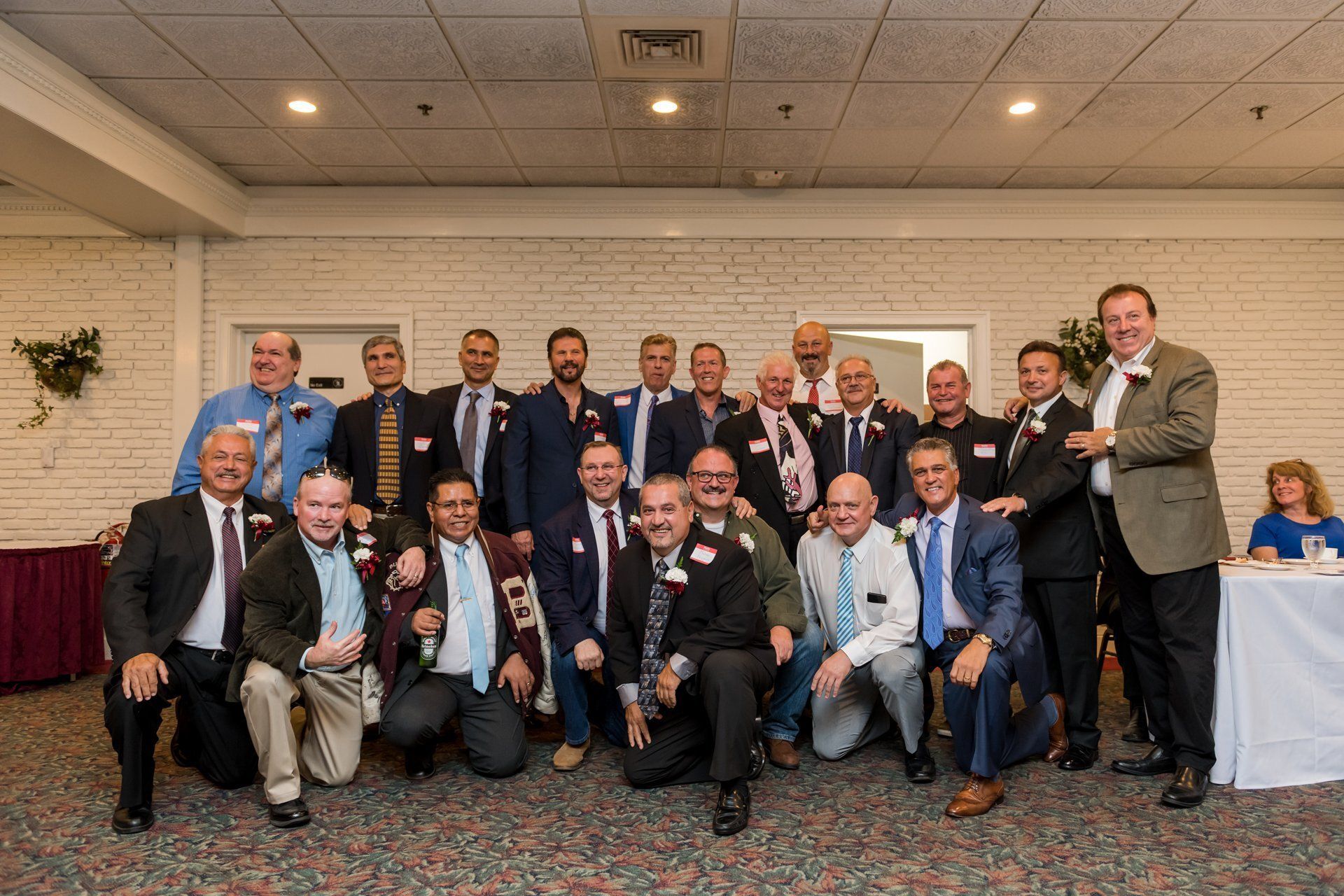 Group of people in suits posing at a banquet hall, smiling for a formal event photo