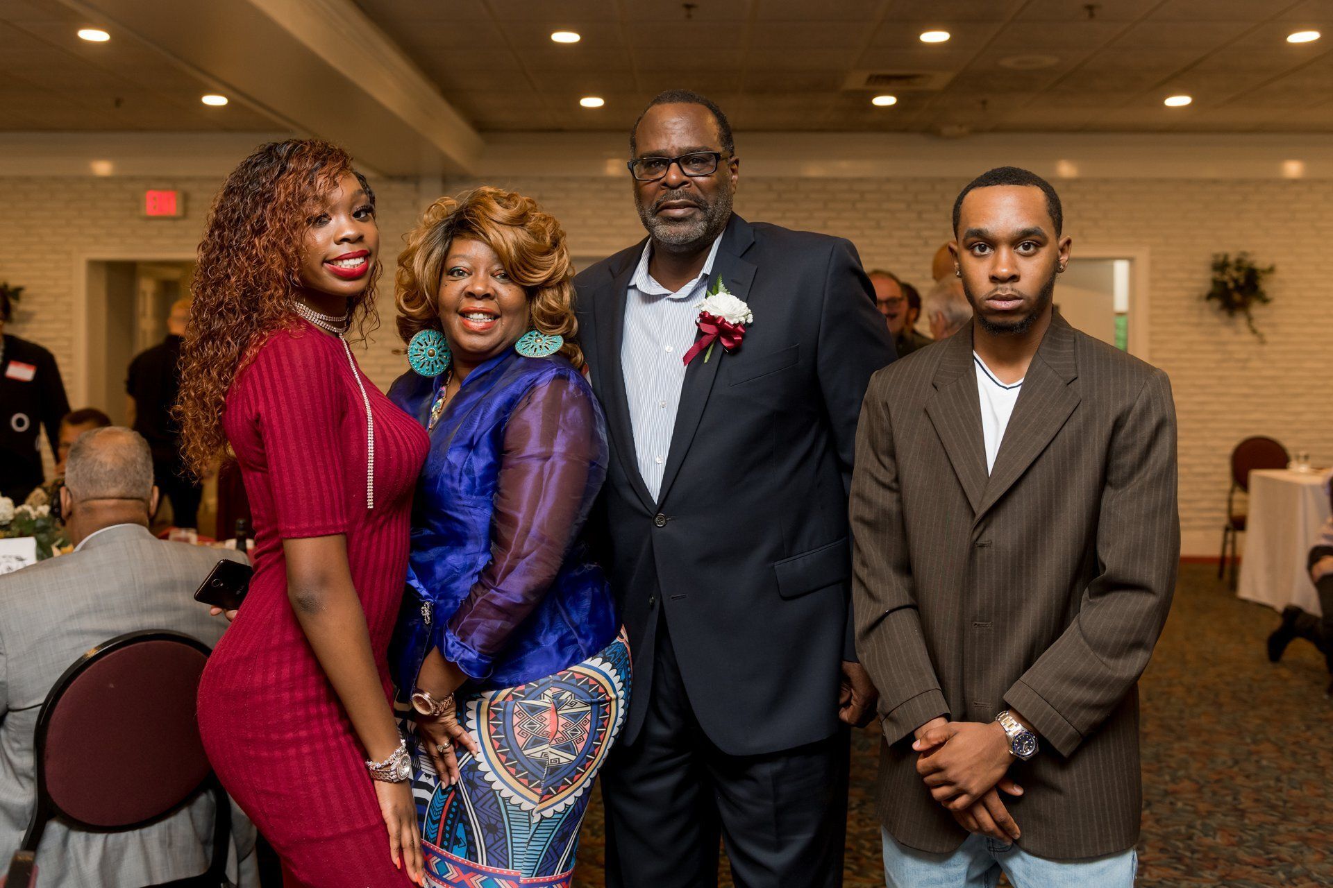 Four people pose in formal attire at an indoor event, with tables and banquet hall decor in the background.