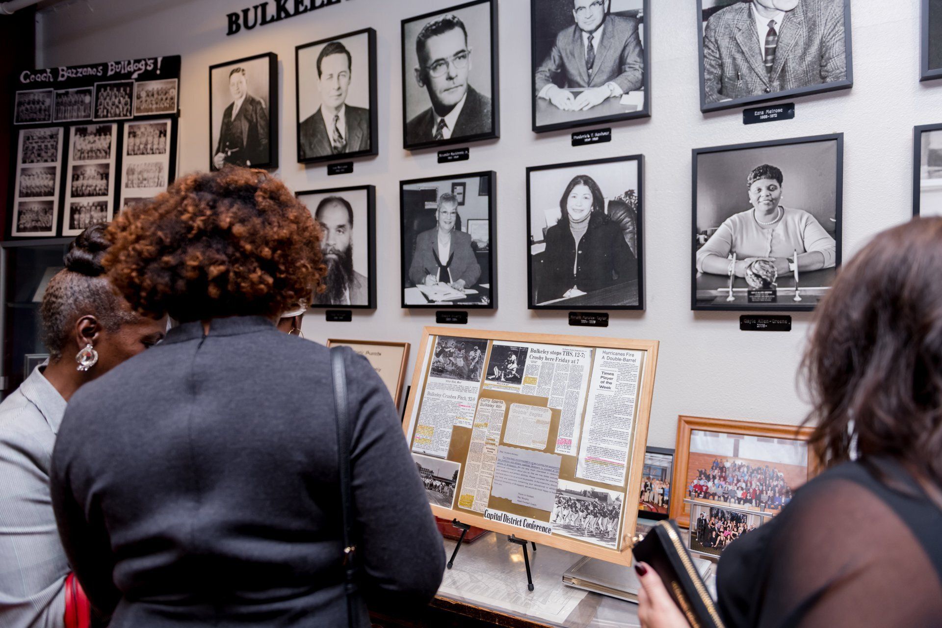 Visitors view framed photos and historical displays in a museum exhibit room.