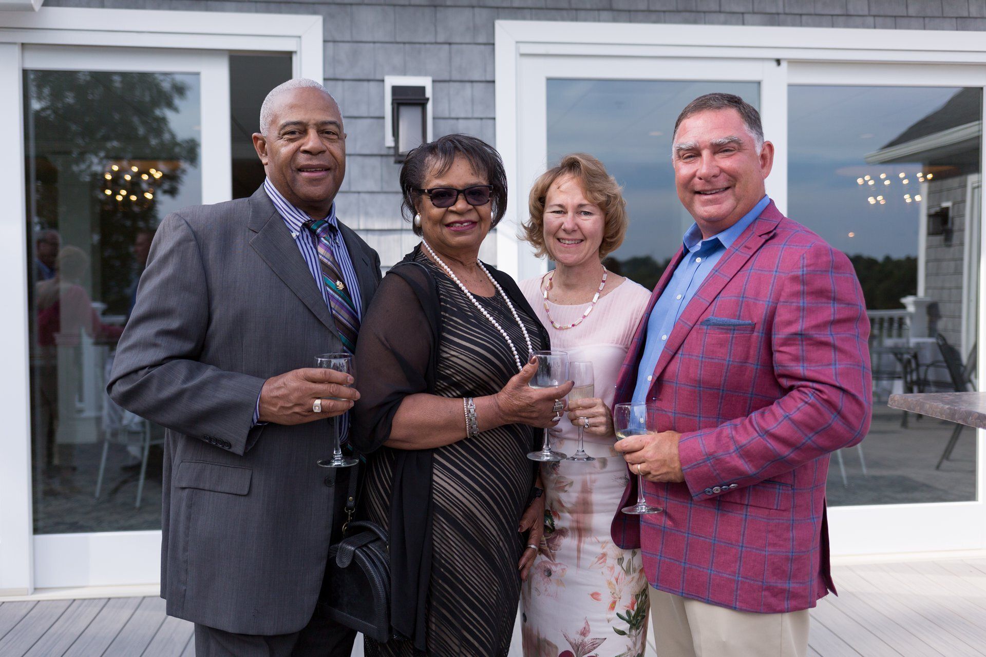 Four guests posing with drinks outside a building entrance, dressed in formal attire.