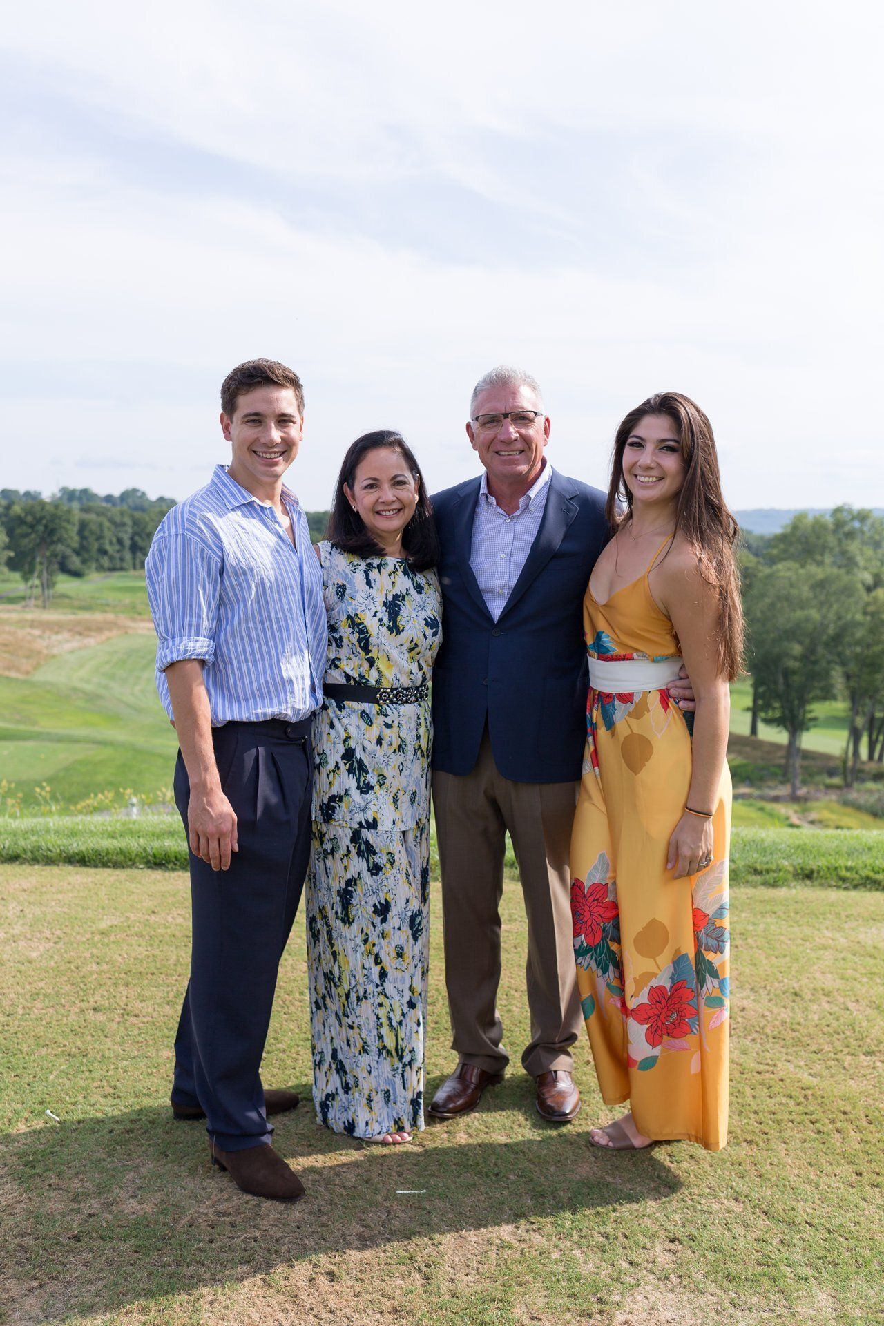 Four people posing together on a grassy hillside under a bright sky.