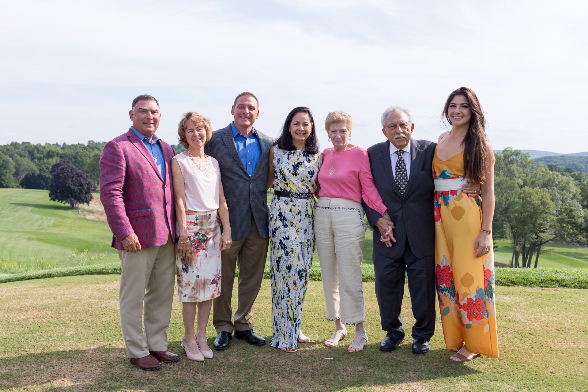 Seven people posing on a golf course, with rolling green hills in the background.