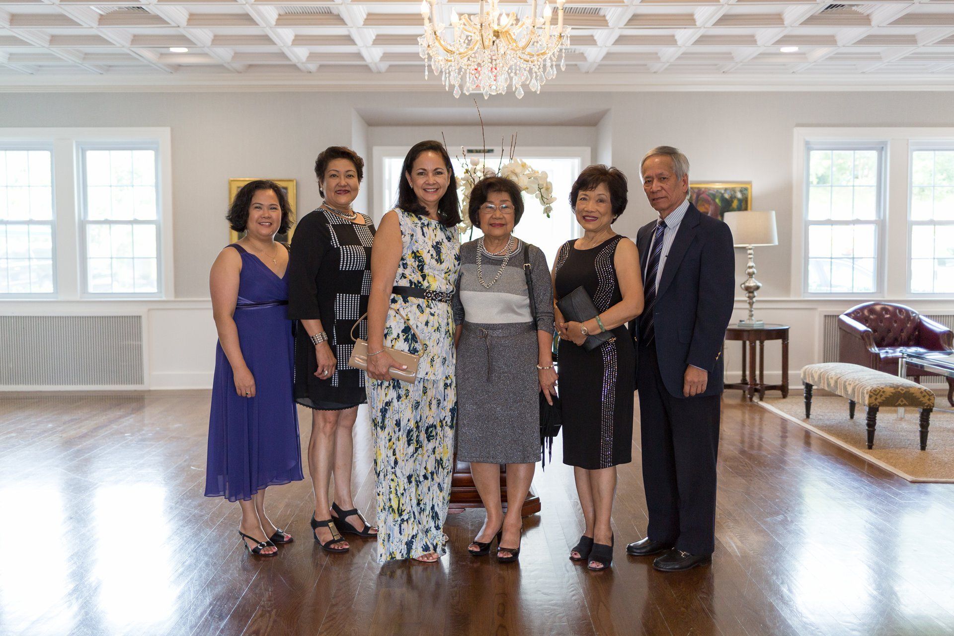 Six people posing in a bright ballroom with chandeliers and polished wood floors