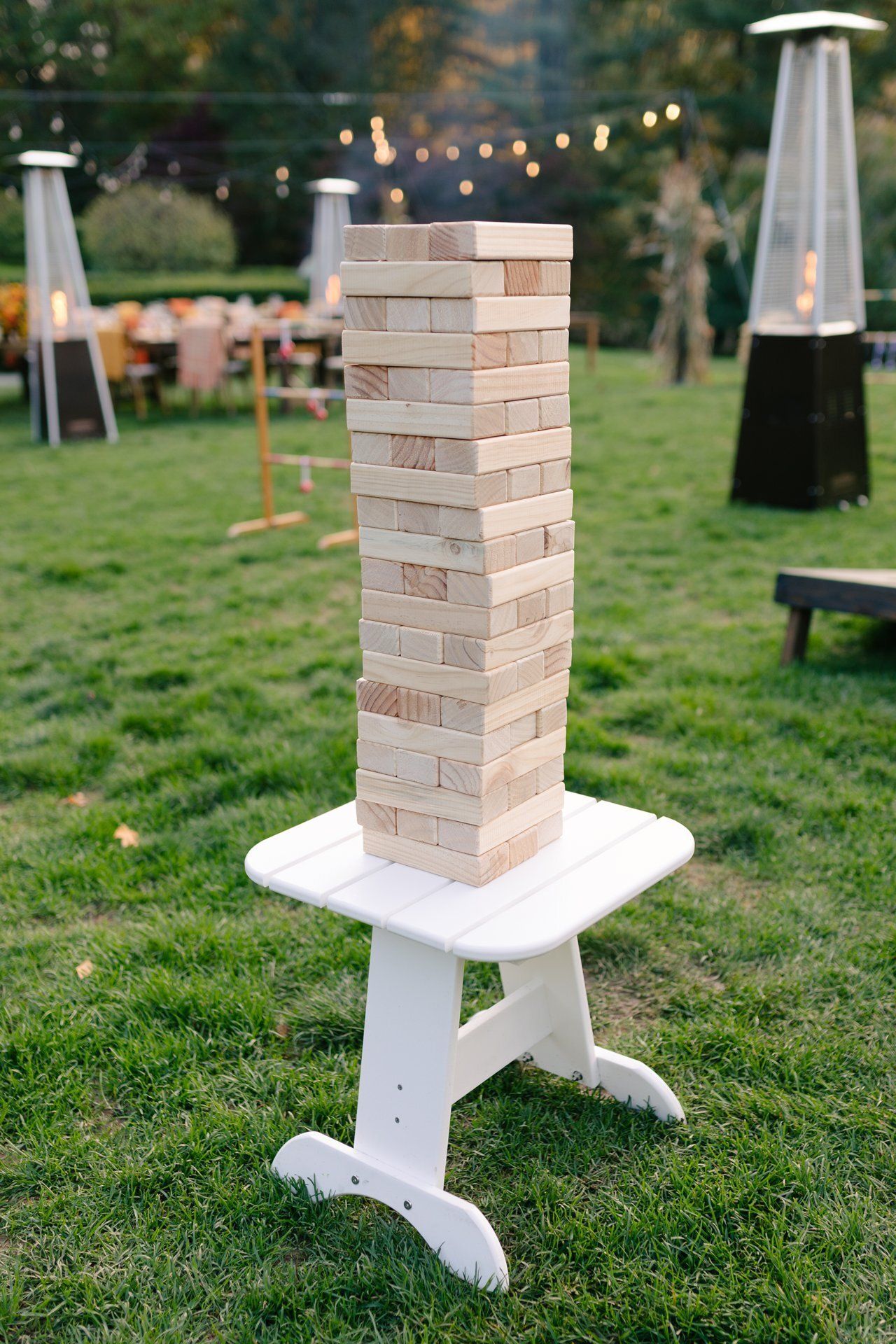 Wooden Jenga tower on a white stool in a grassy outdoor setting.