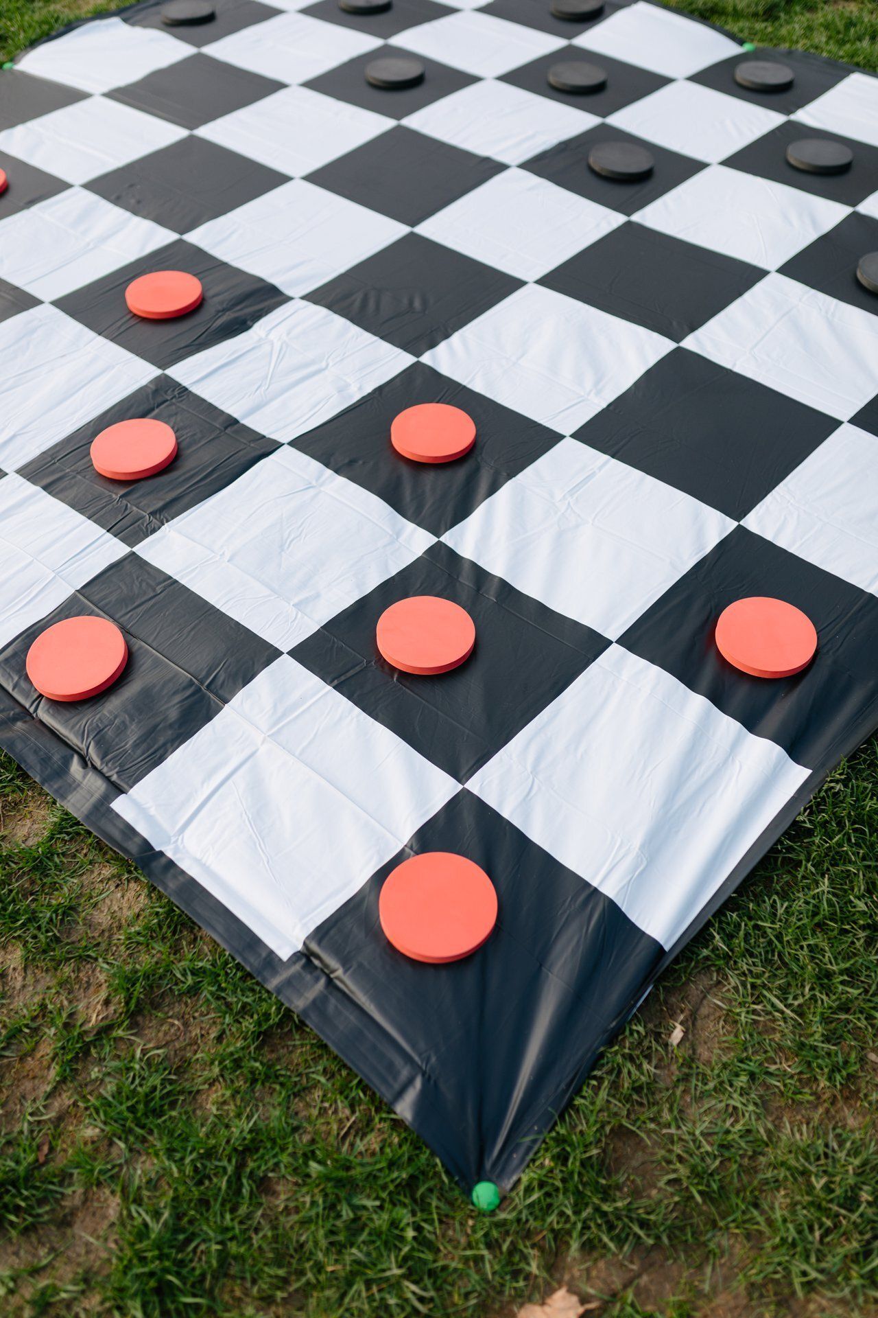 Outdoor giant checkerboard game with black and white squares and red and black pieces on grass