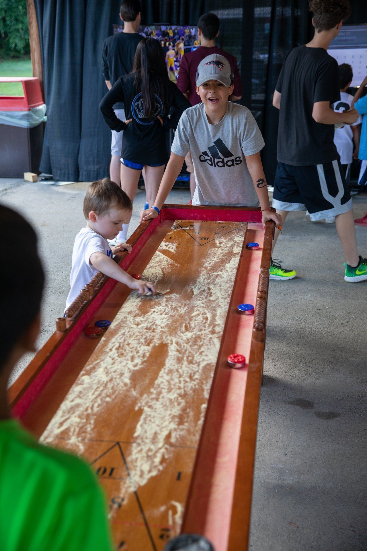 Children playing with a sand-filled wooden tray game at an outdoor event.